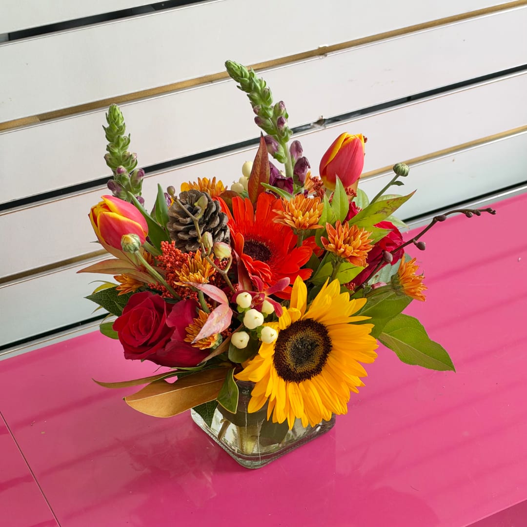 Colorful mixed bouquet in a square glass vase with sunflowers, roses, and tulips