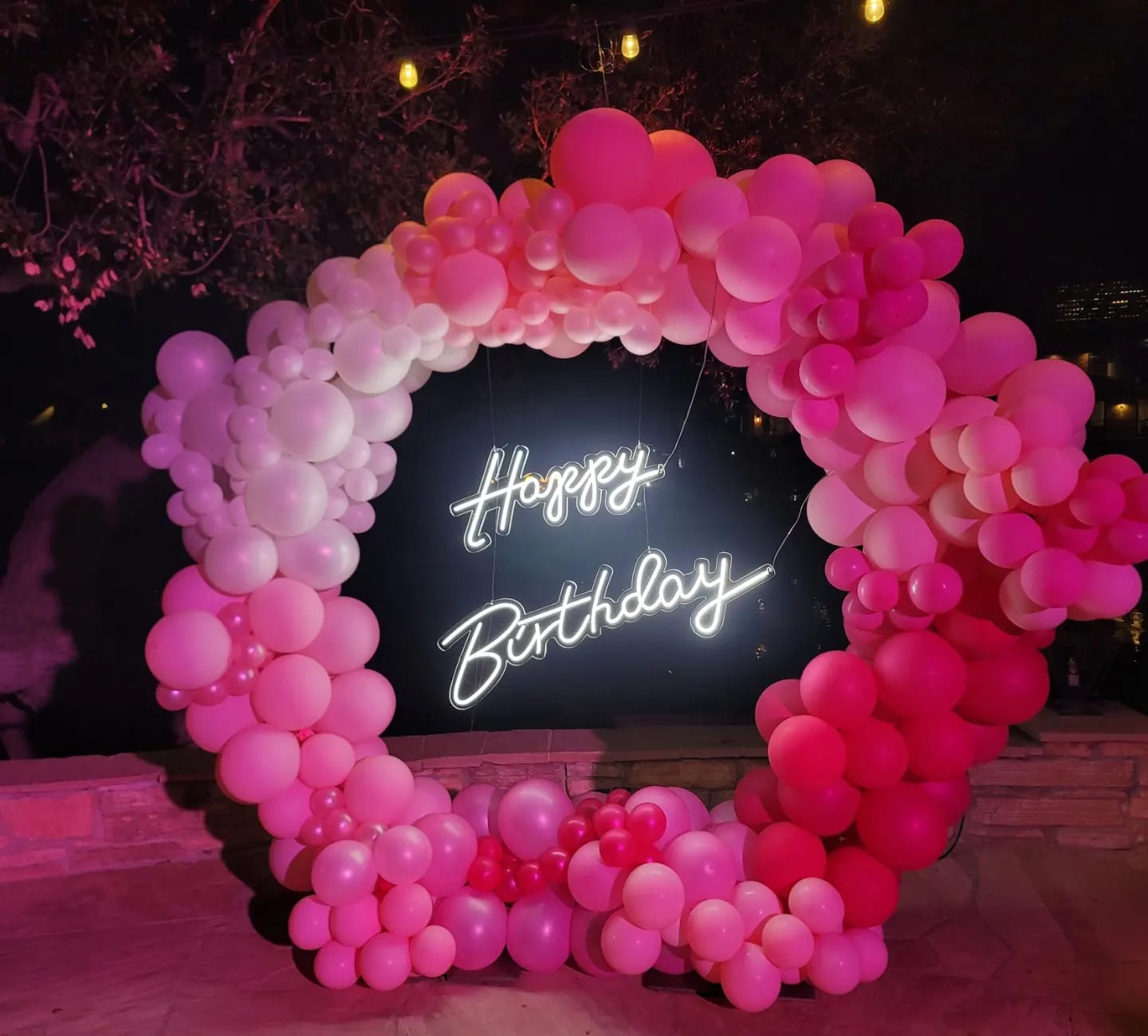 Pink balloon arch around a neon Happy Birthday sign