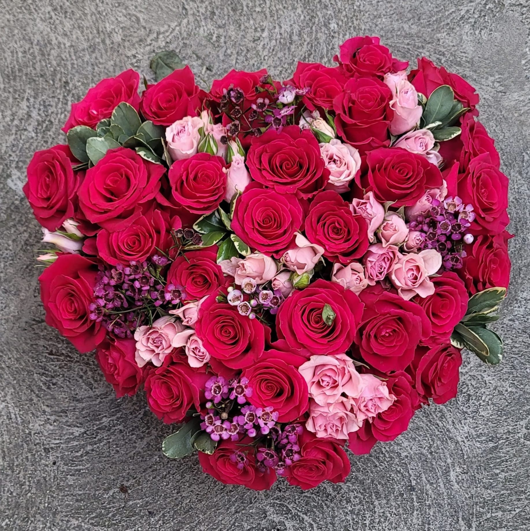 Heart-shaped bouquet of pink and red roses with small purple accents