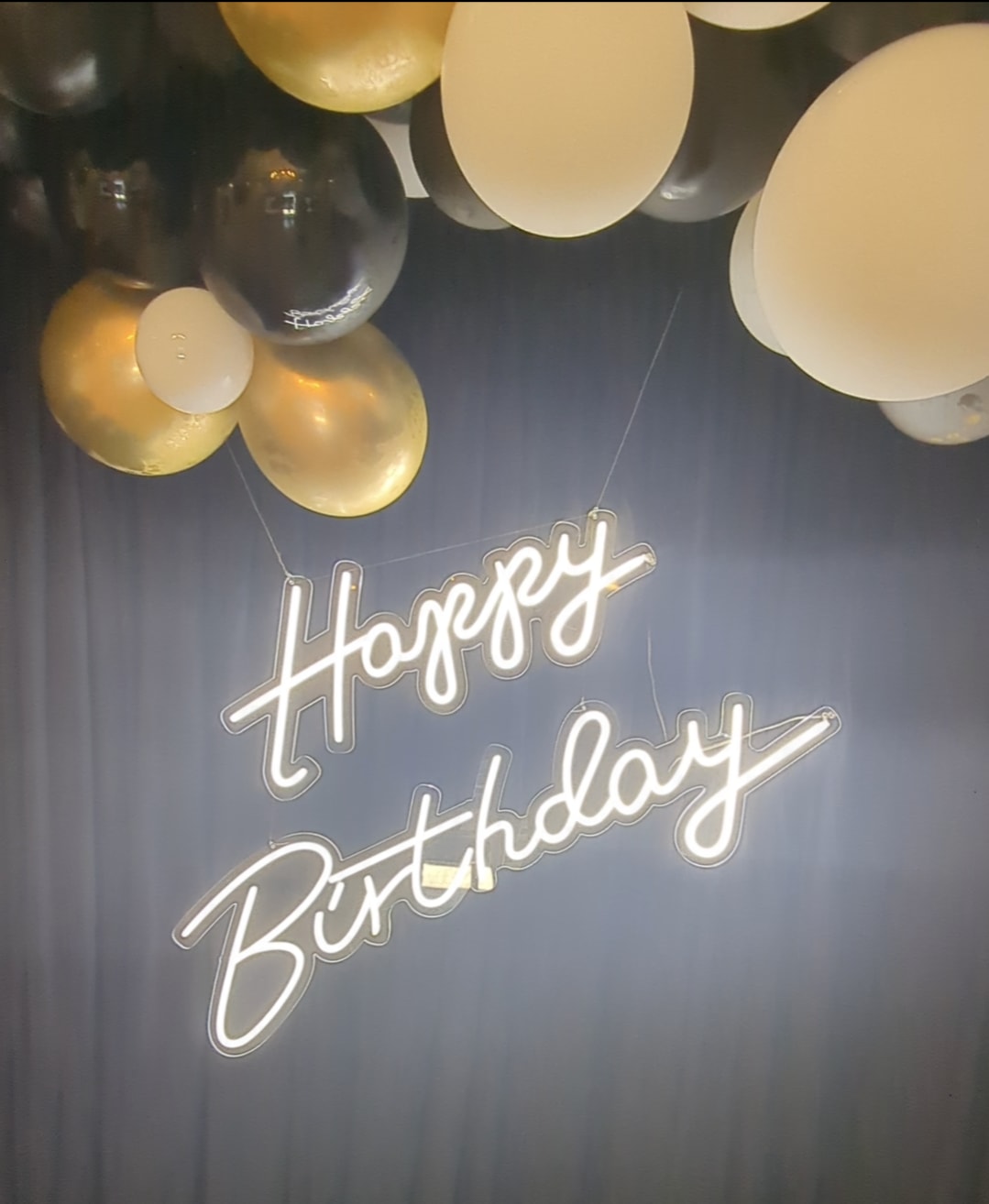 Birthday sign with gold, black, and white balloons overhead