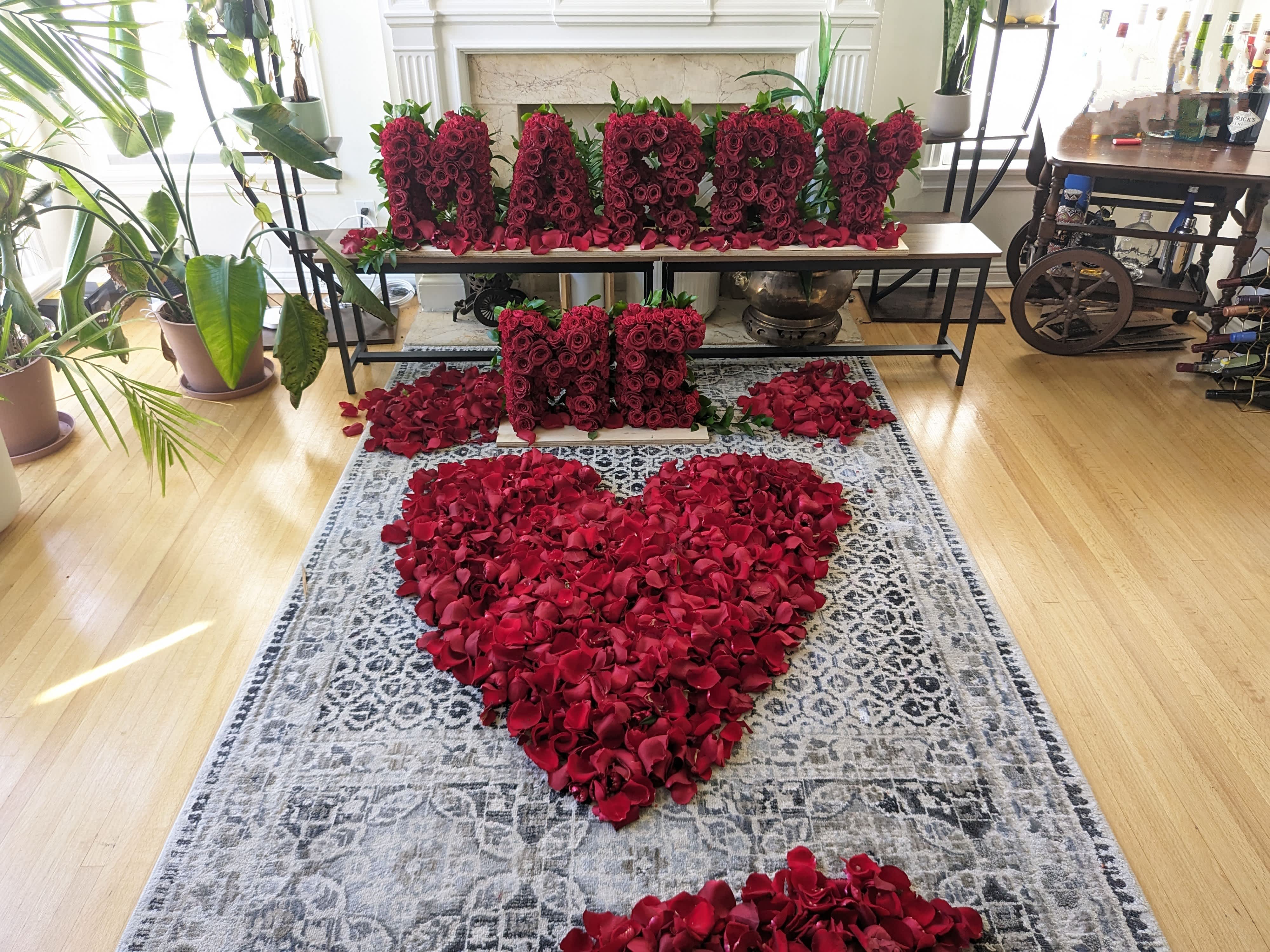 Red rose petals arranged in a heart shape with rose letter blocks on a table