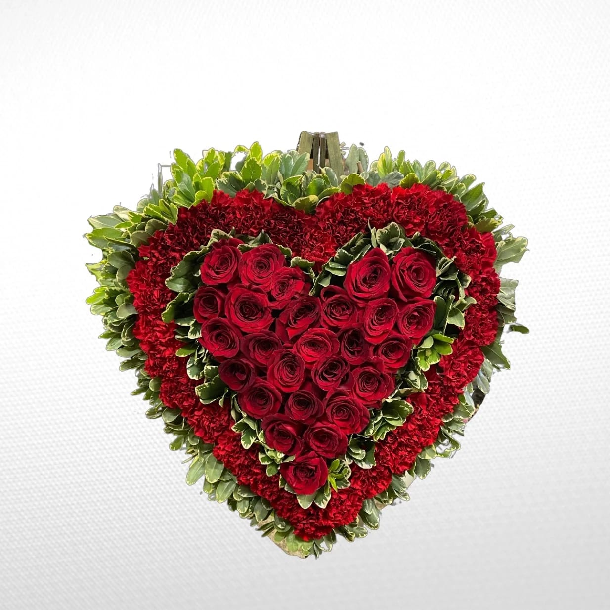 Heart-shaped arrangement of red roses and carnations with green foliage