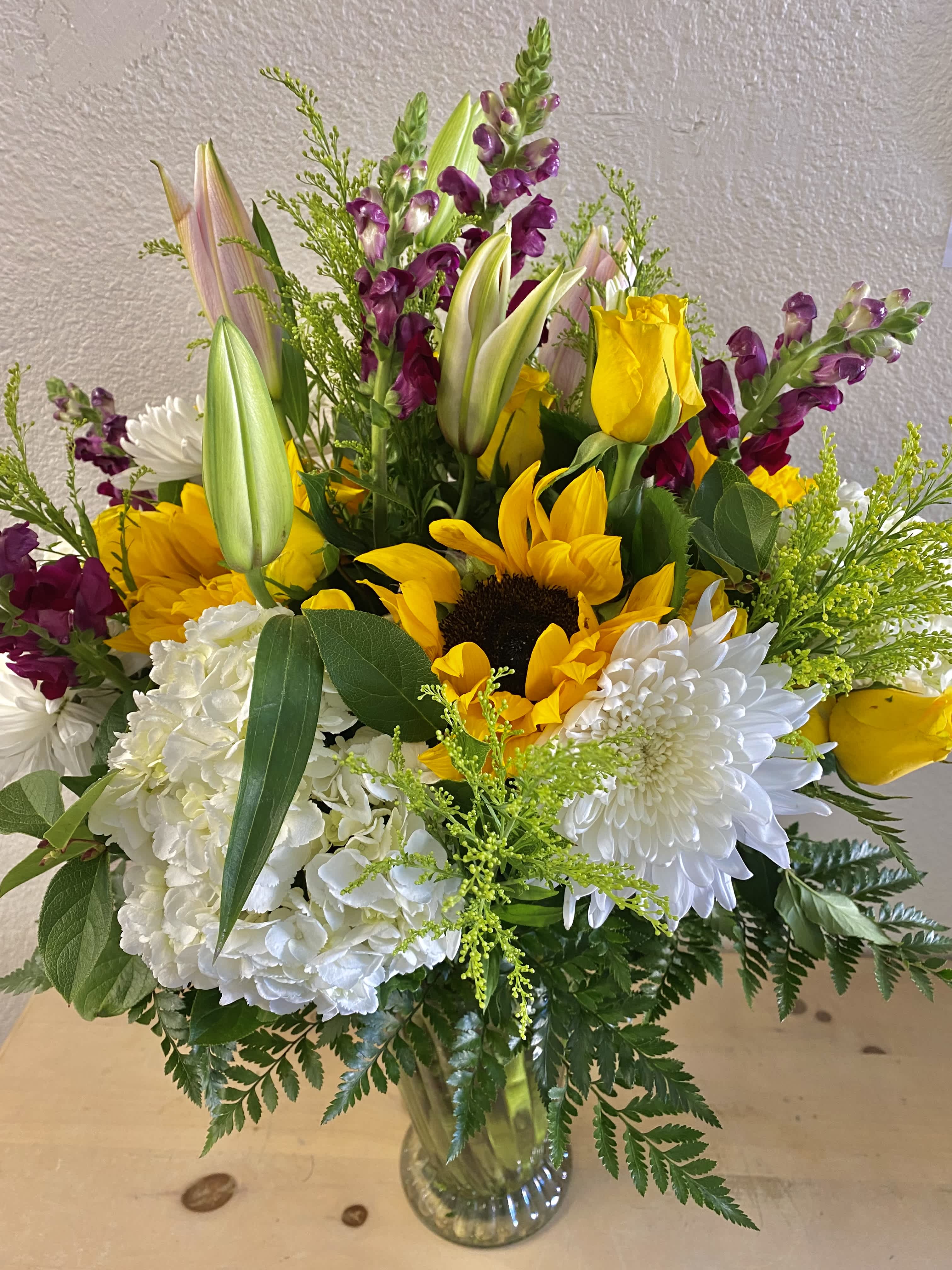 Bouquet of sunflowers, white chrysanthemums, and purple snapdragons in a glass vase