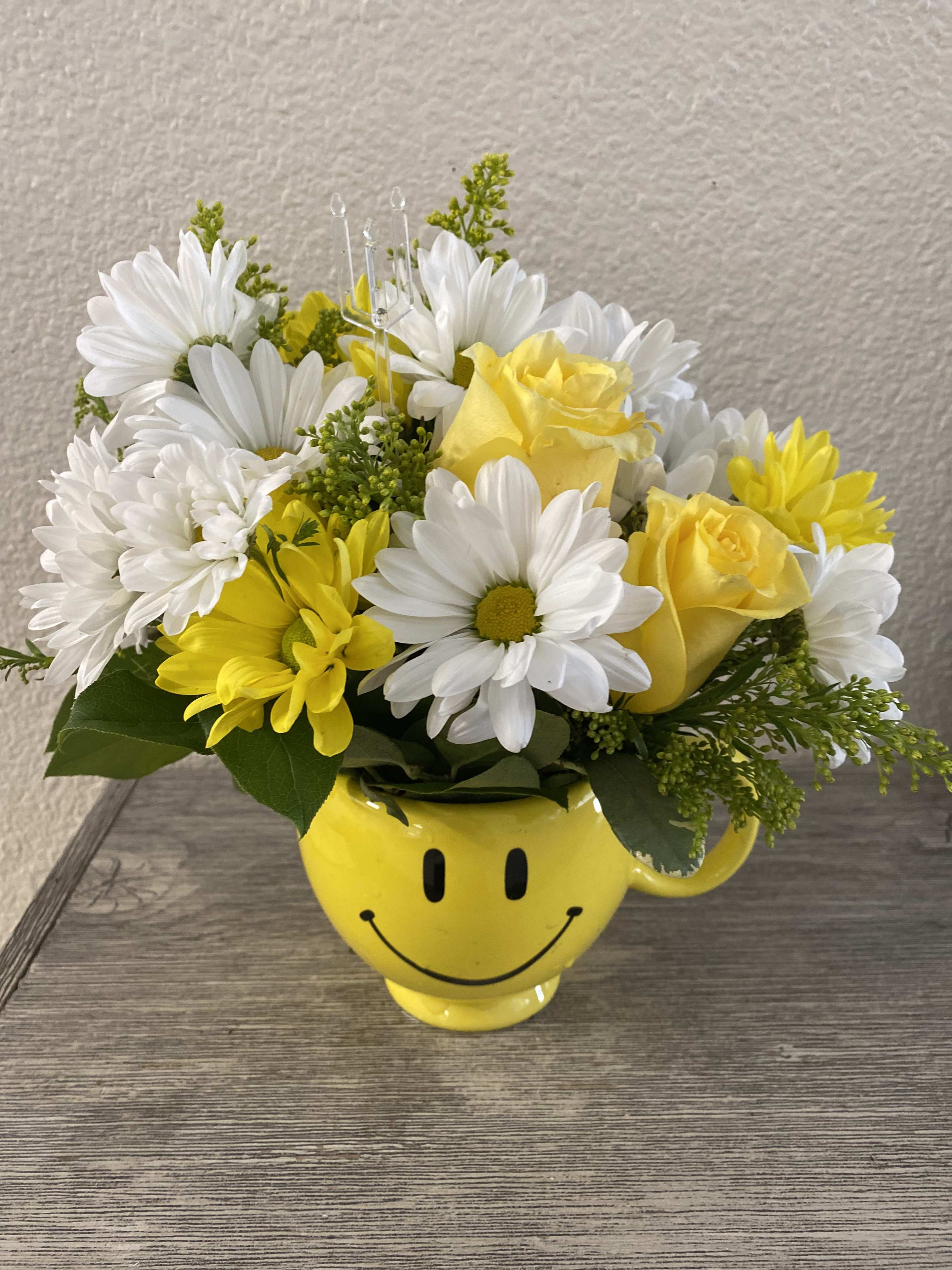 Yellow and white flowers arranged in a smiley-face mug