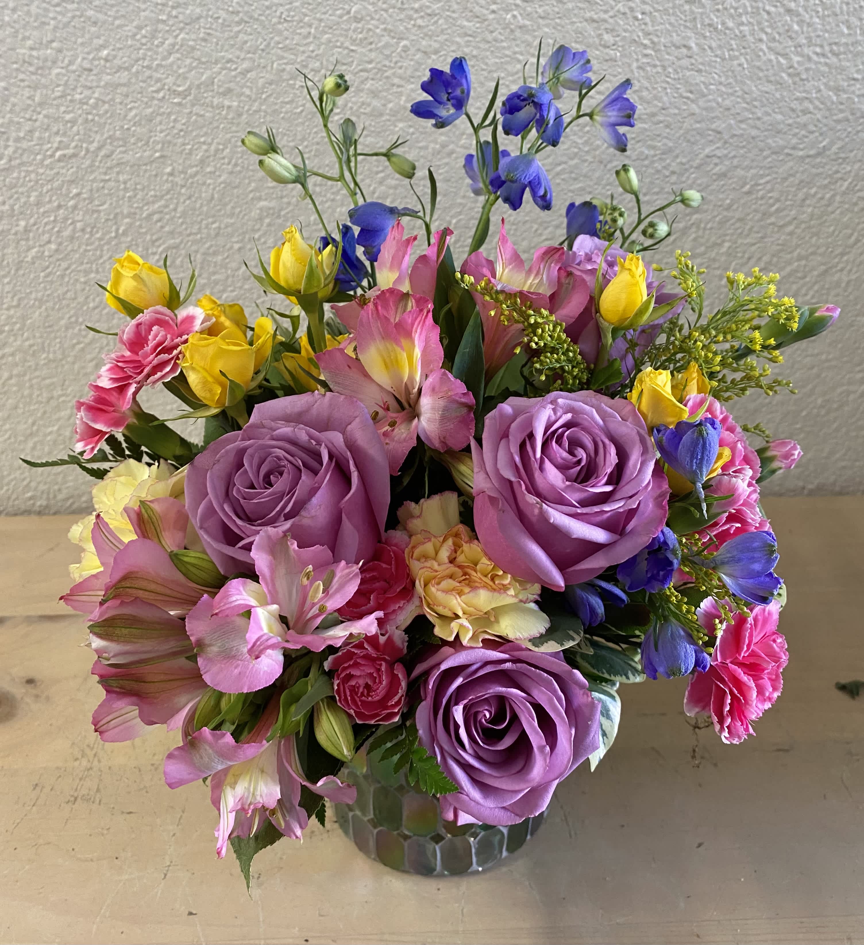 Mixed bouquet of purple roses, pink alstroemeria, and yellow blooms in a glass vase