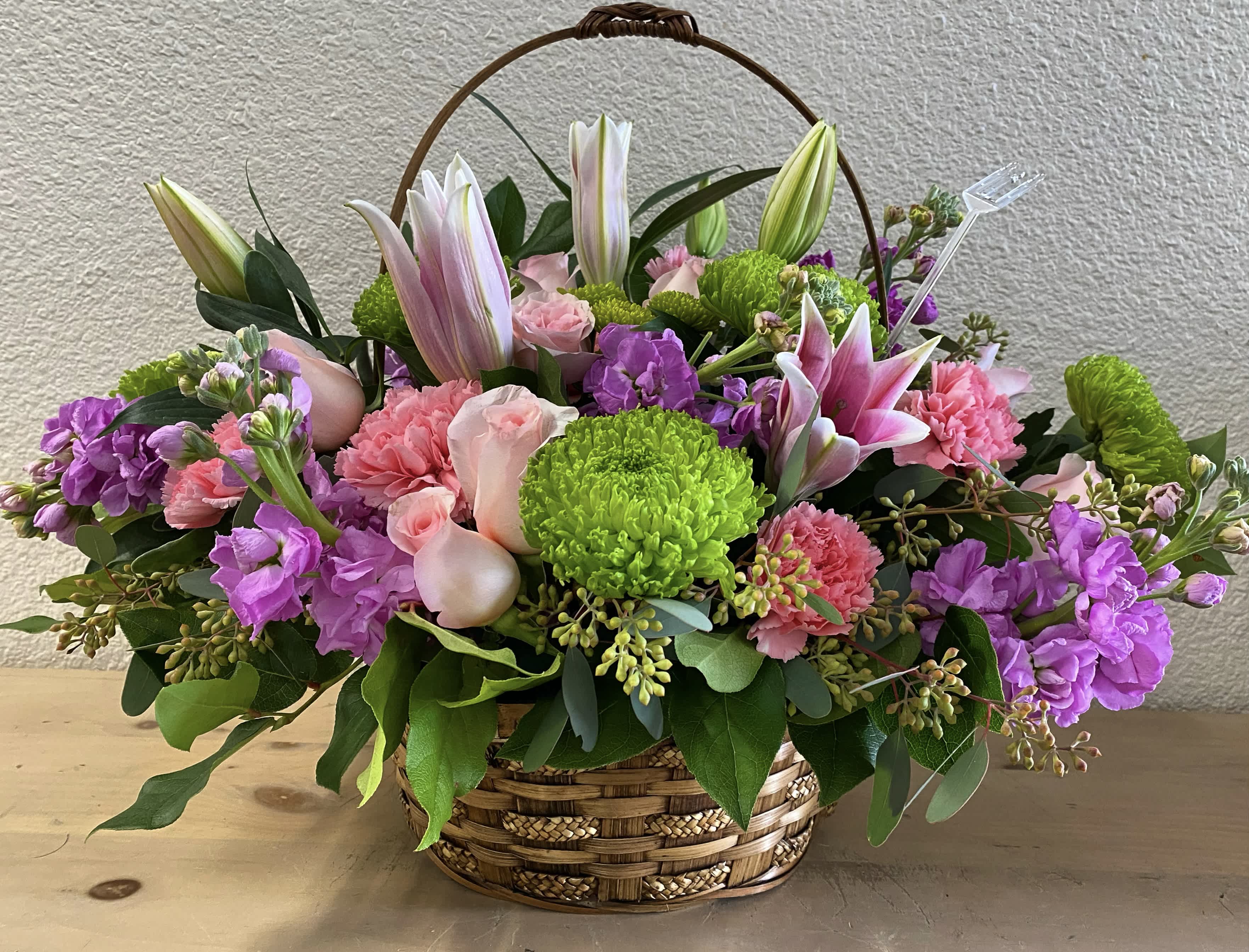 Basket arrangement with pink lilies, roses, carnations, and purple blooms