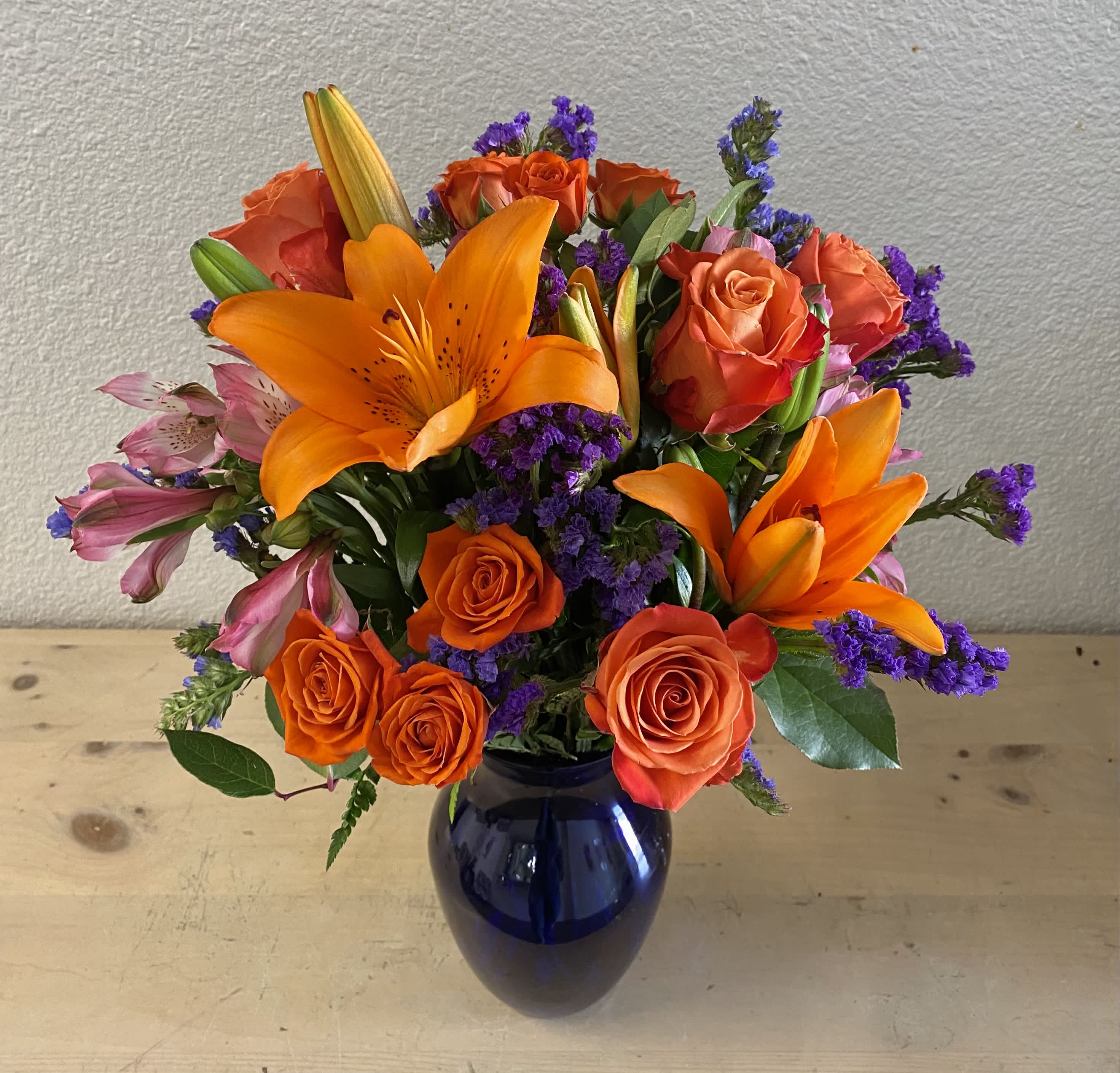 Orange lilies and roses in a blue vase with purple filler flowers