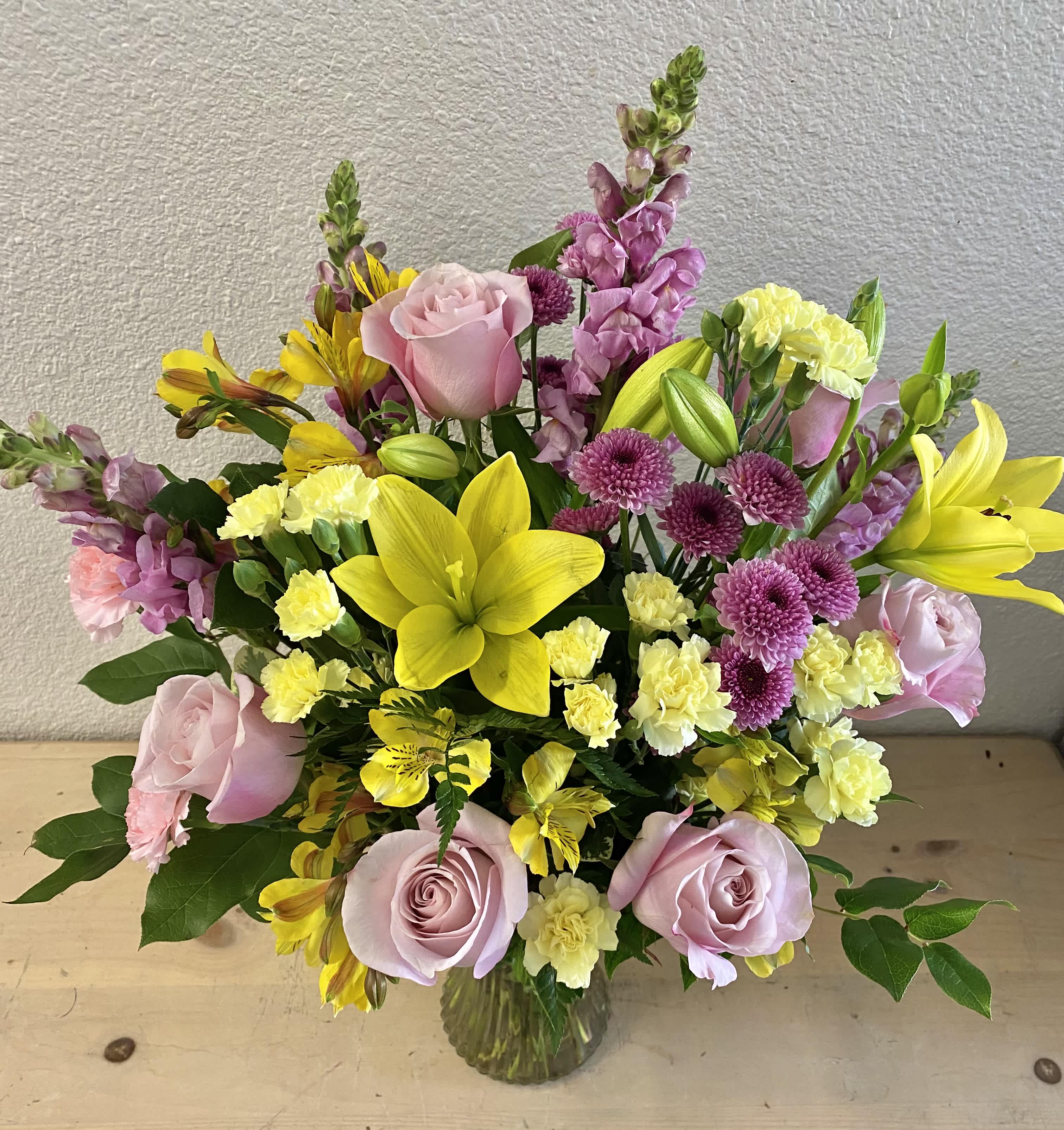 Pink roses, yellow lilies, and purple flowers in a glass vase