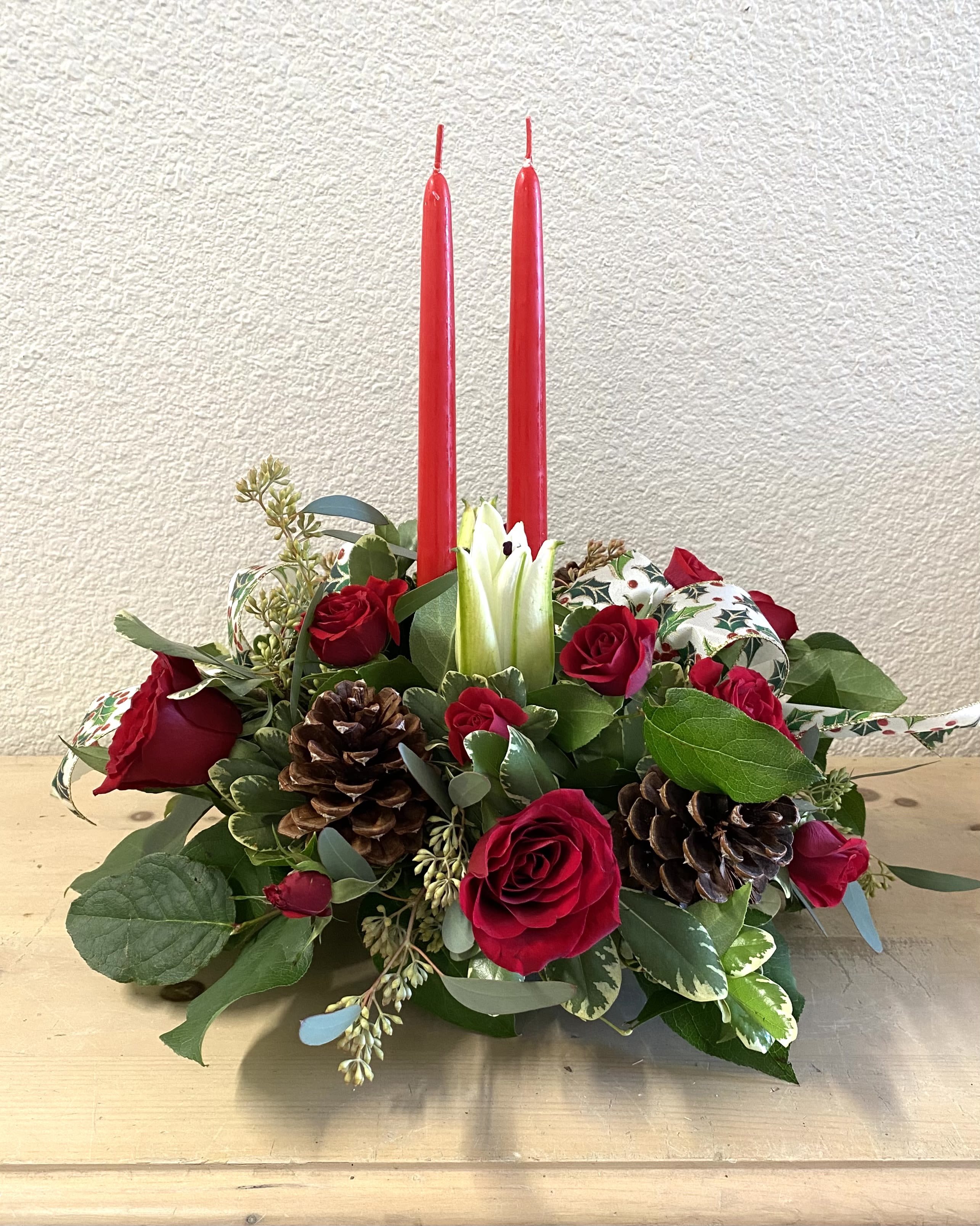 Red roses and pinecones arranged with two tall red candles.