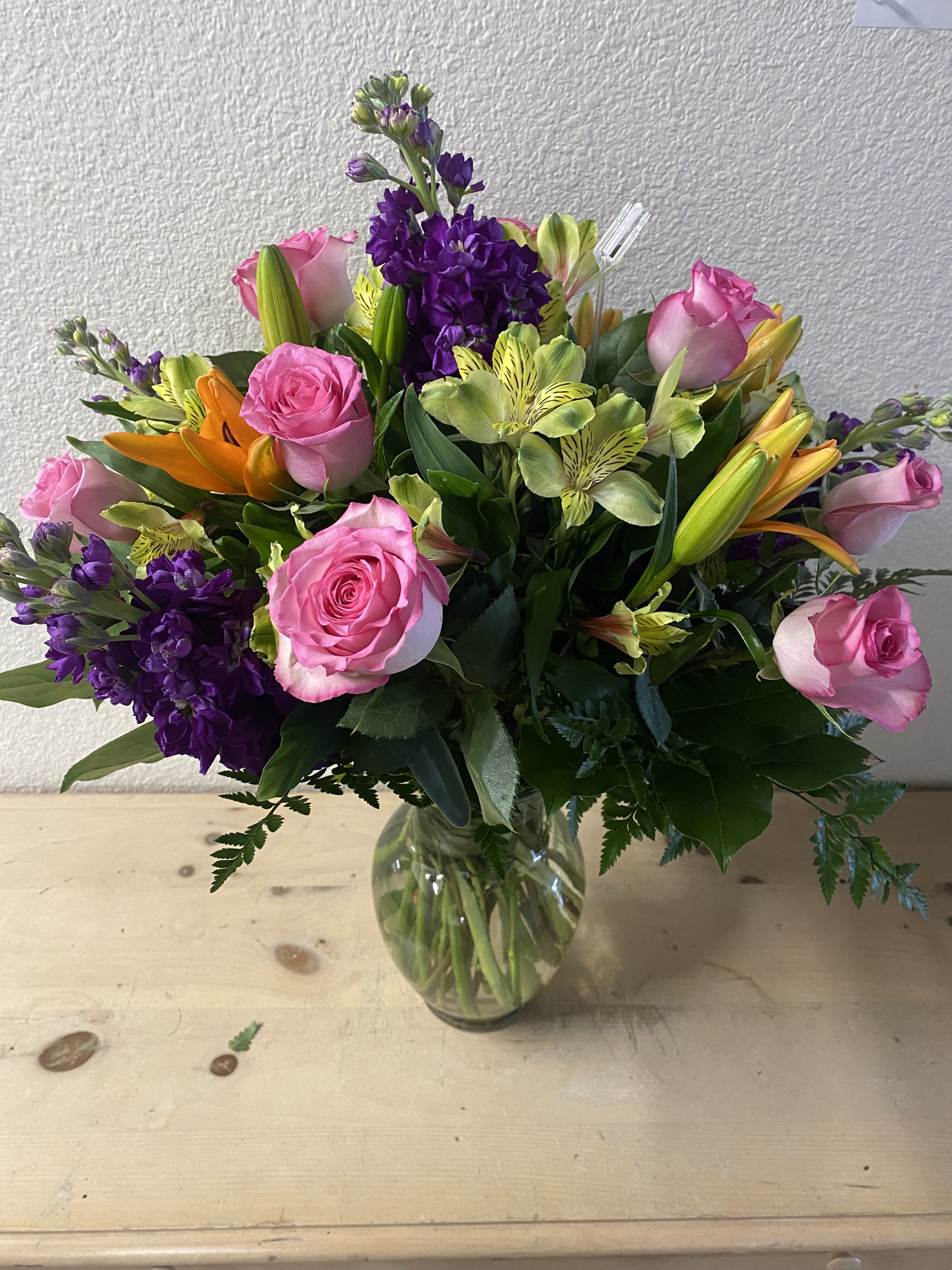Mixed bouquet of pink roses, purple flowers, and lilies in a glass vase