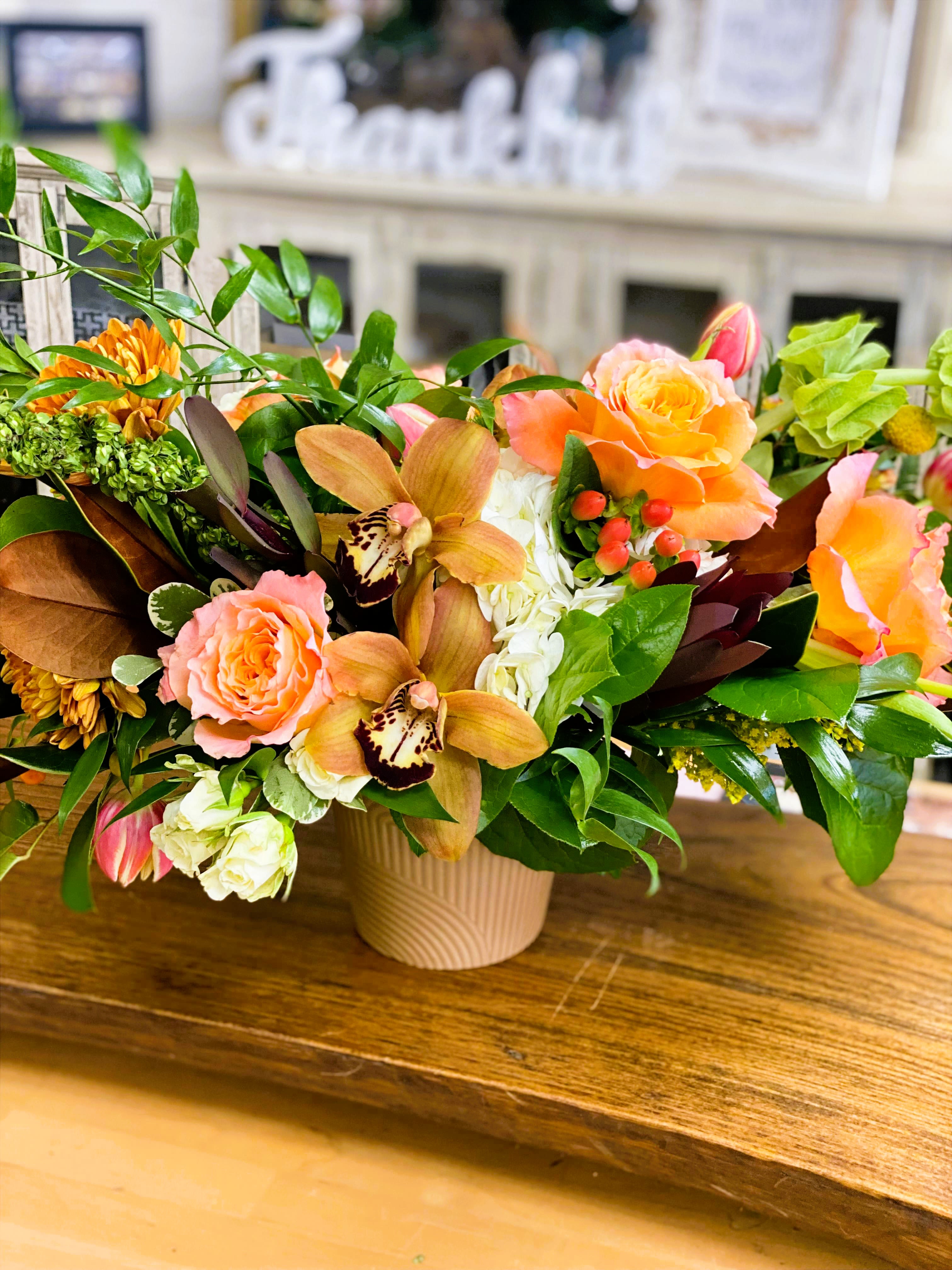 Mixed floral arrangement in a beige vase with peach roses and orchids