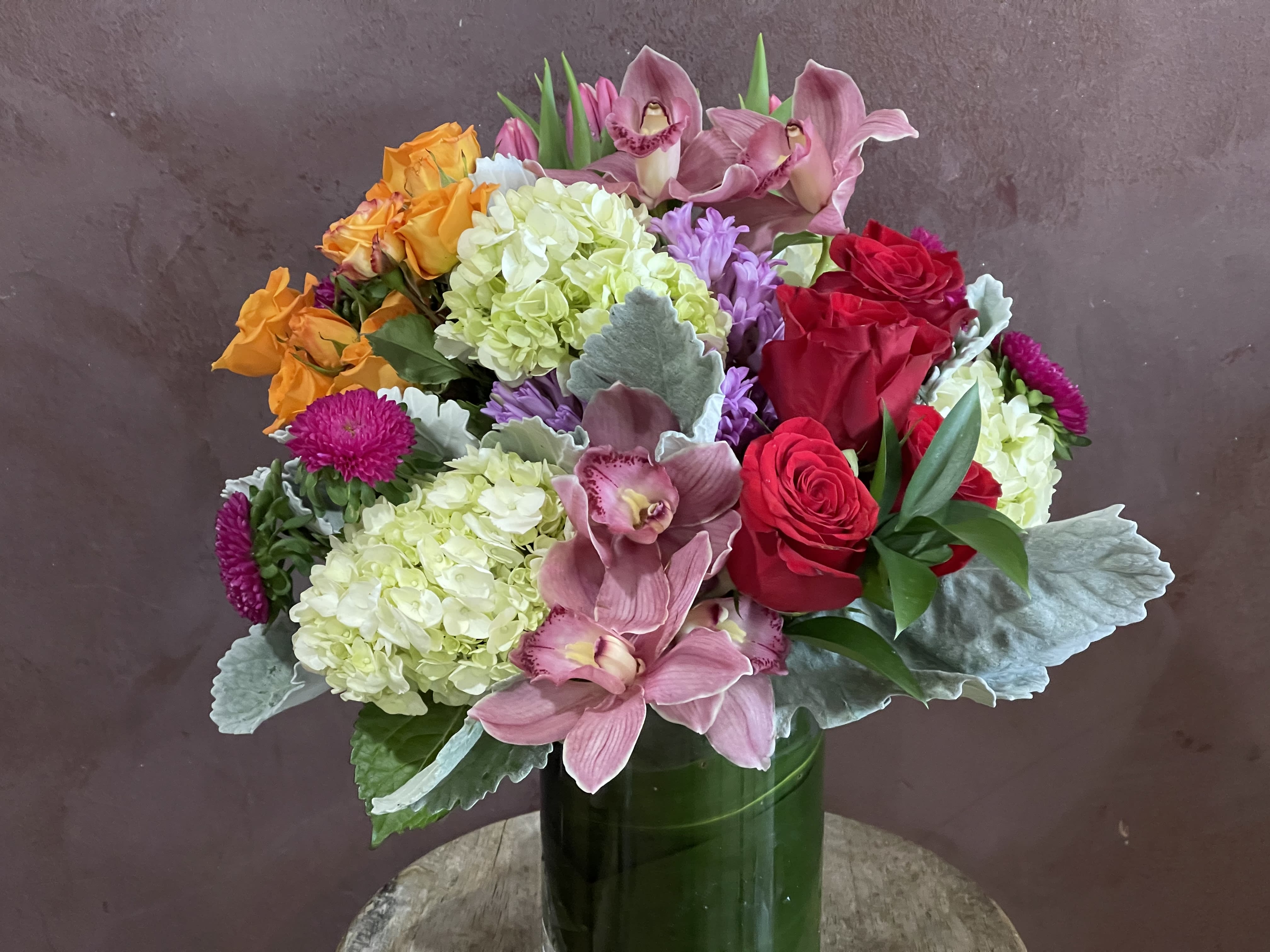 Mixed bouquet of roses, orchids, and hydrangeas in a green vase