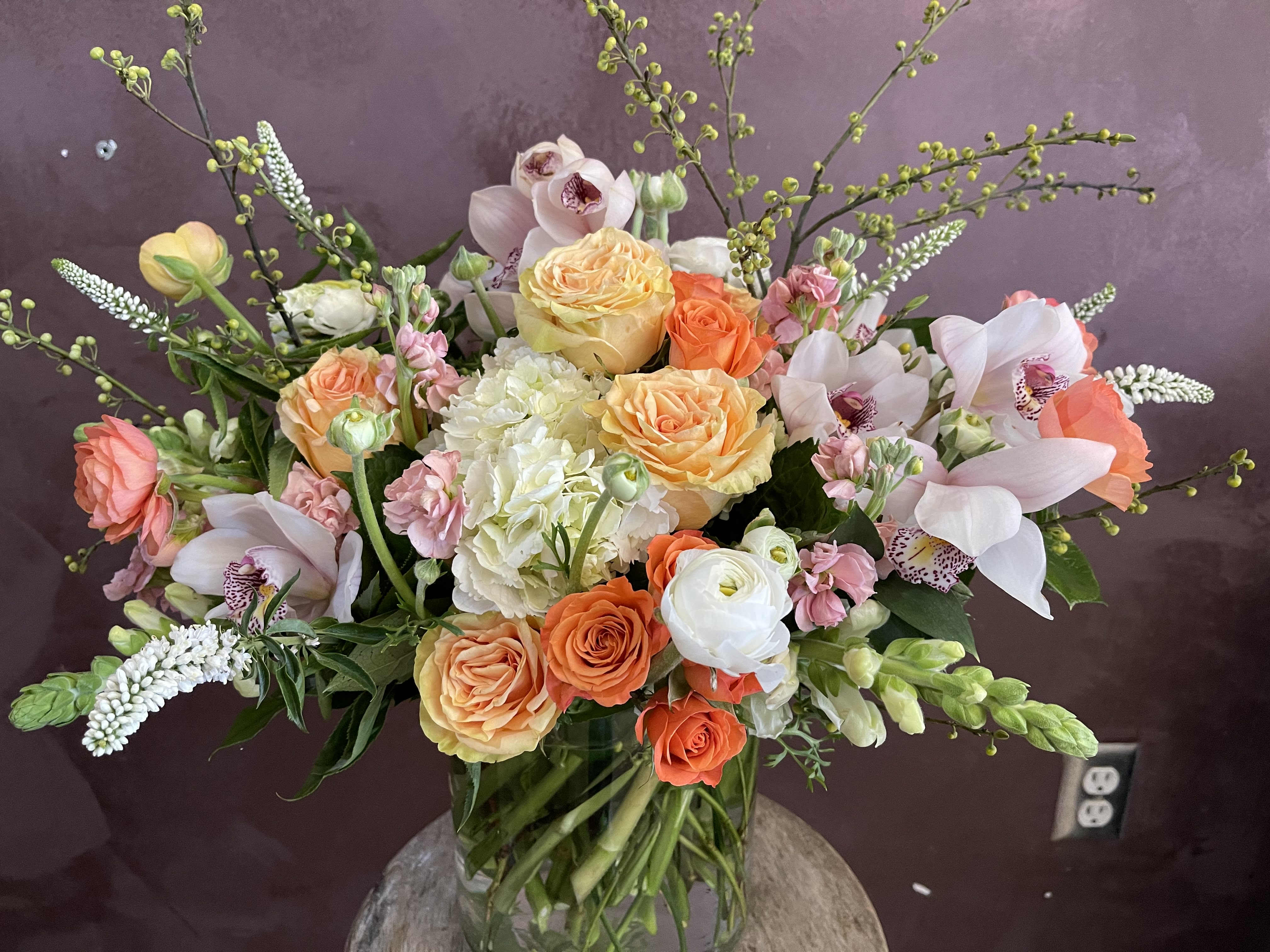 Mixed bouquet of roses, orchids, and hydrangea in a glass vase