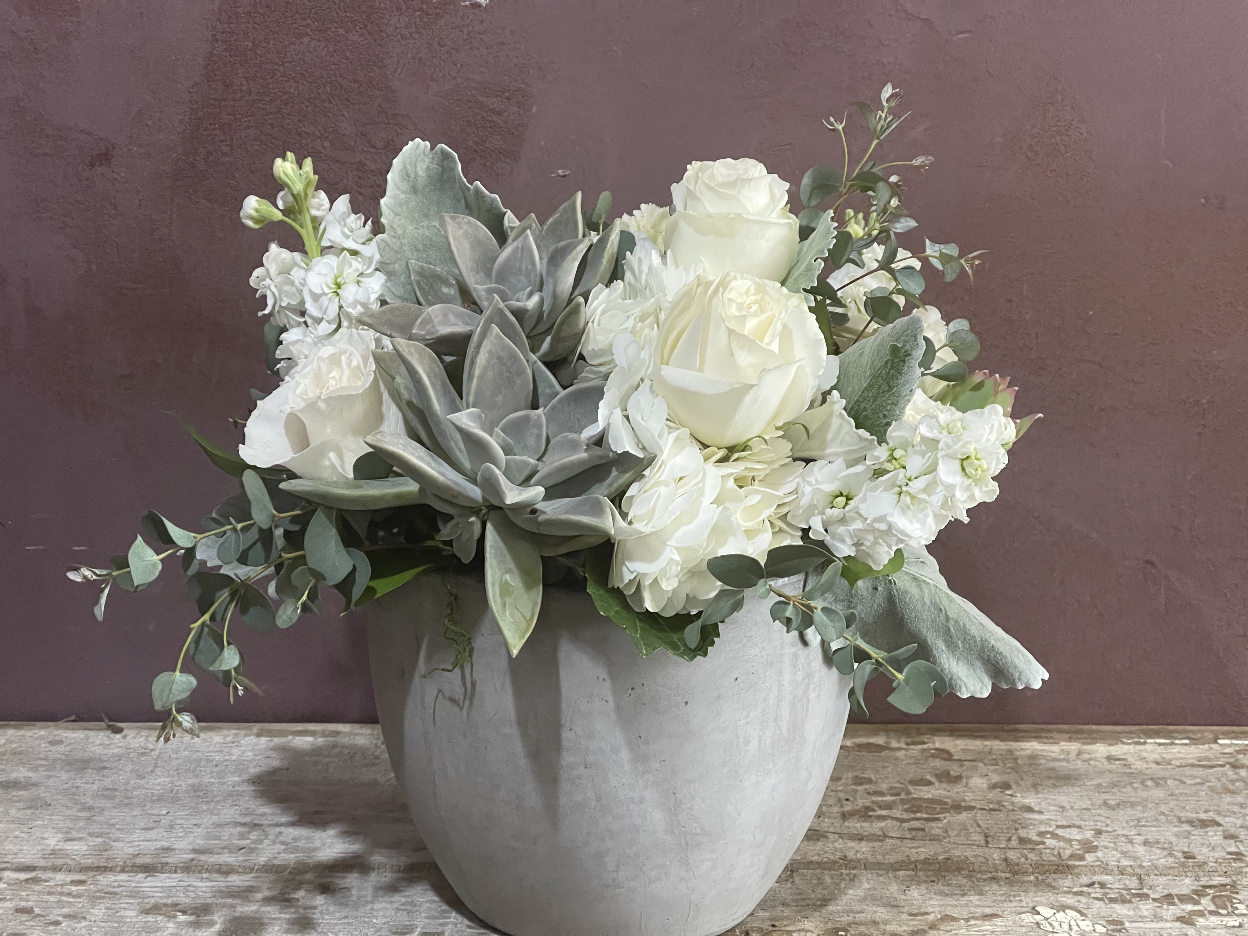 White roses and succulents arranged in a gray pot
