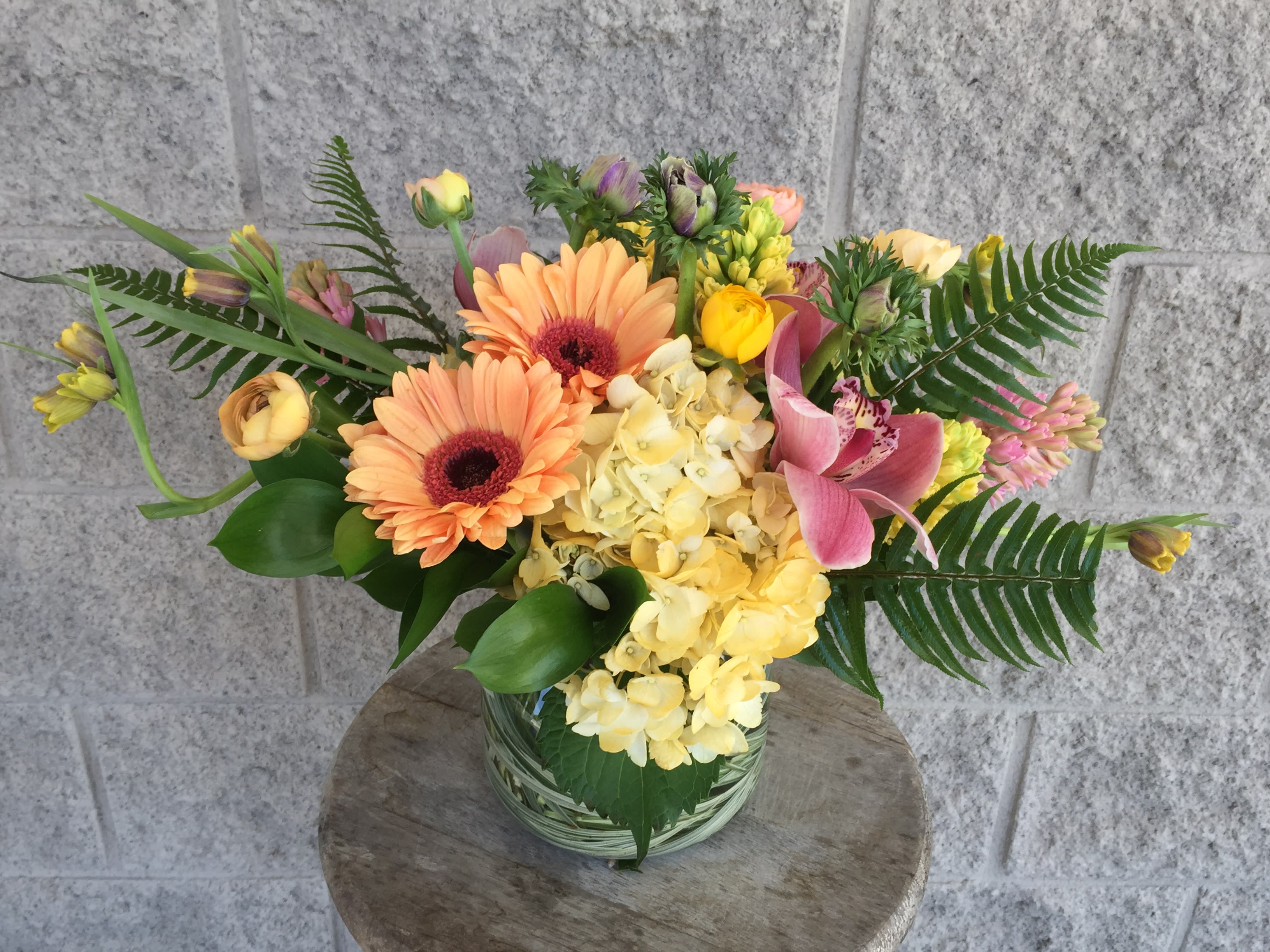 Mixed bouquet with peach gerberas, yellow hydrangea, and pink calla lilies in a glass vase