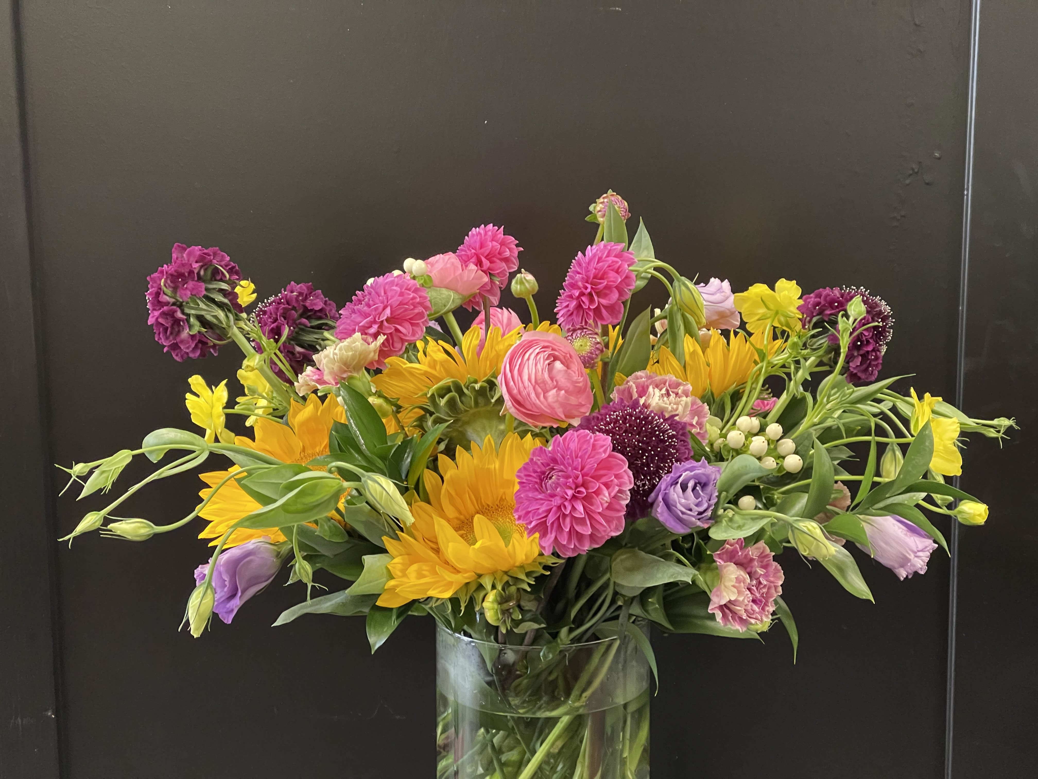 Mixed bouquet of pink, yellow, and purple flowers in a glass vase