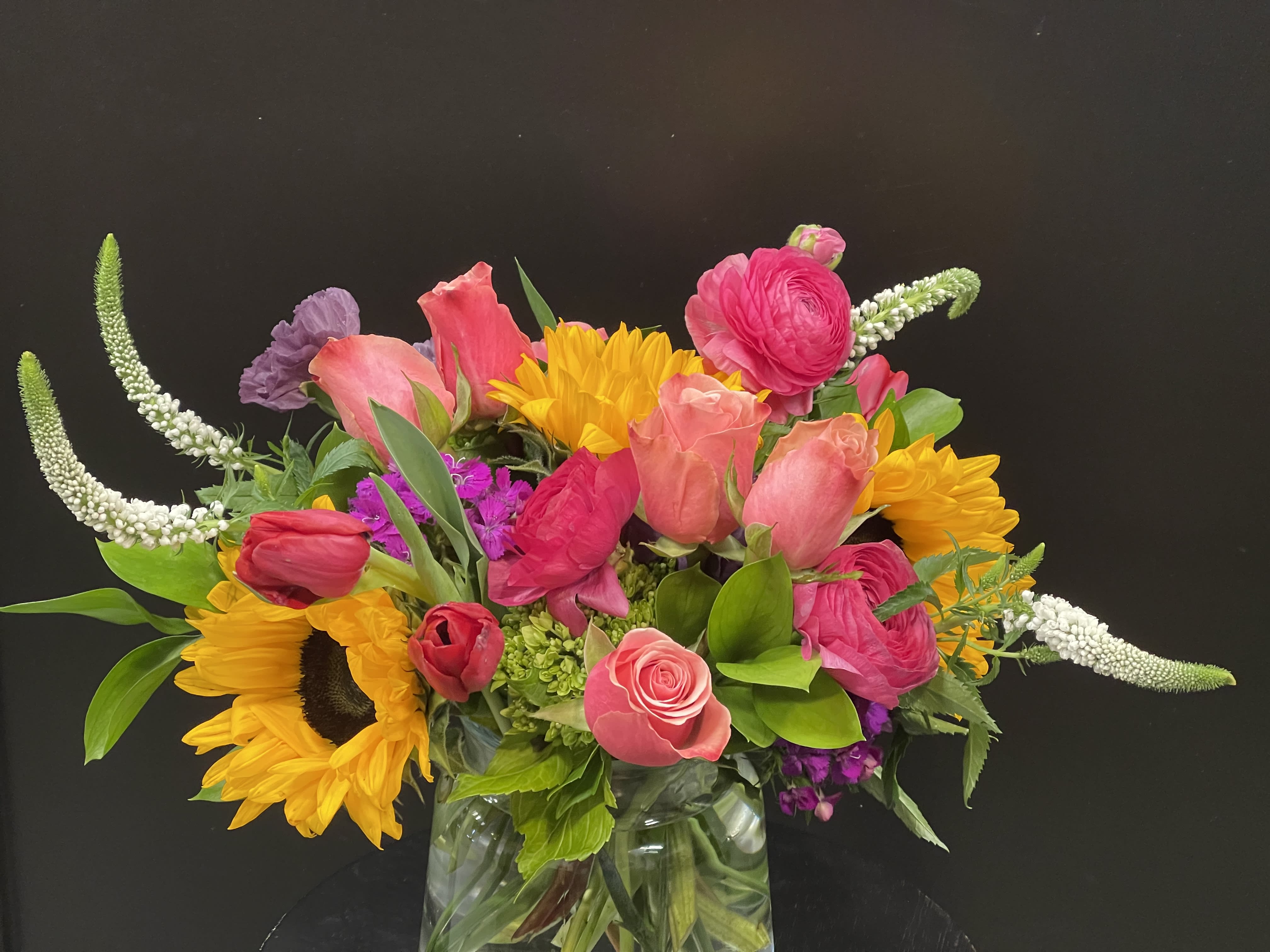 Colorful mixed bouquet with sunflowers, pink roses, and tulips in a glass vase