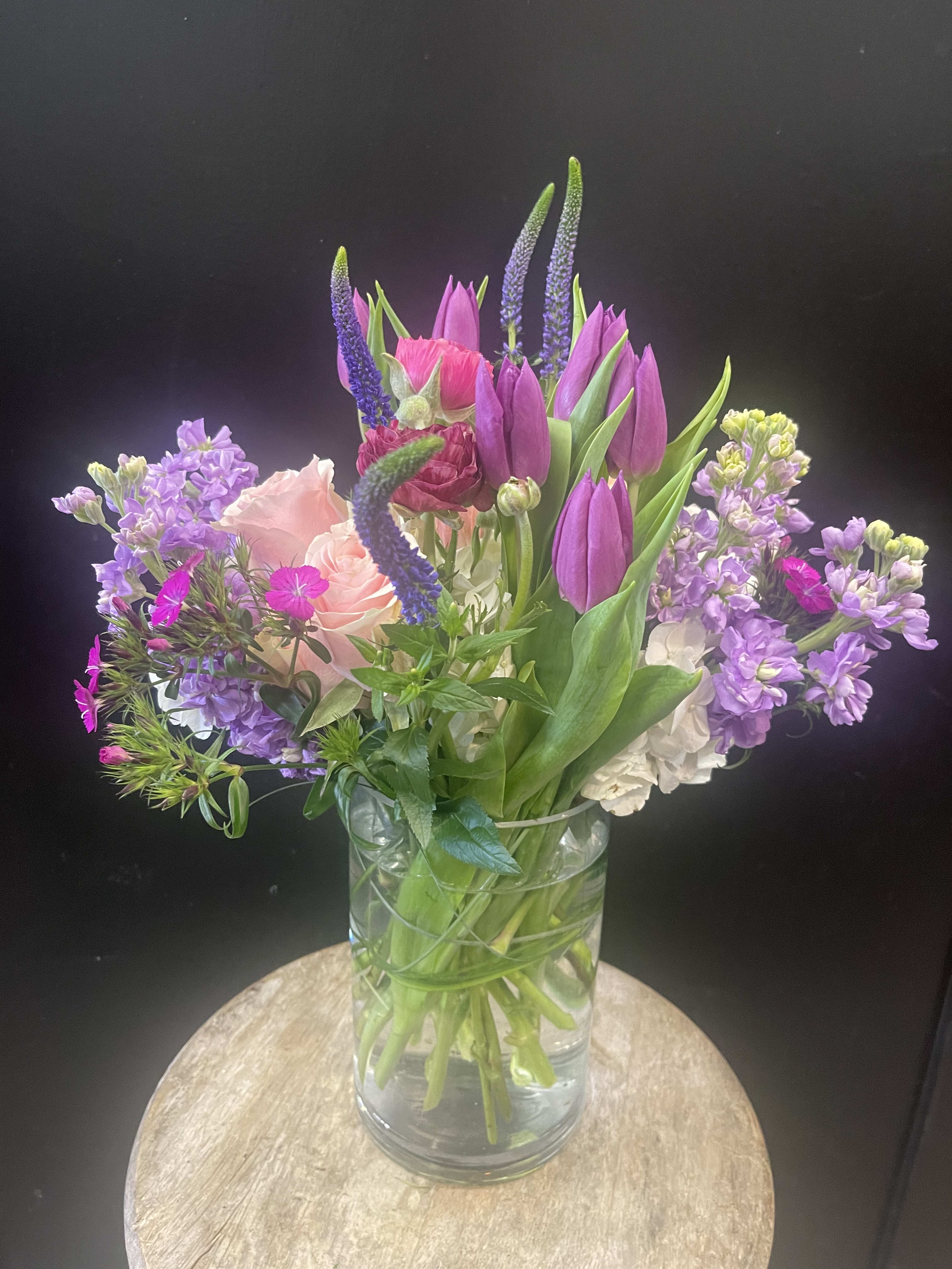 Mixed bouquet of purple tulips, pink roses, and lavender flowers in a glass vase
