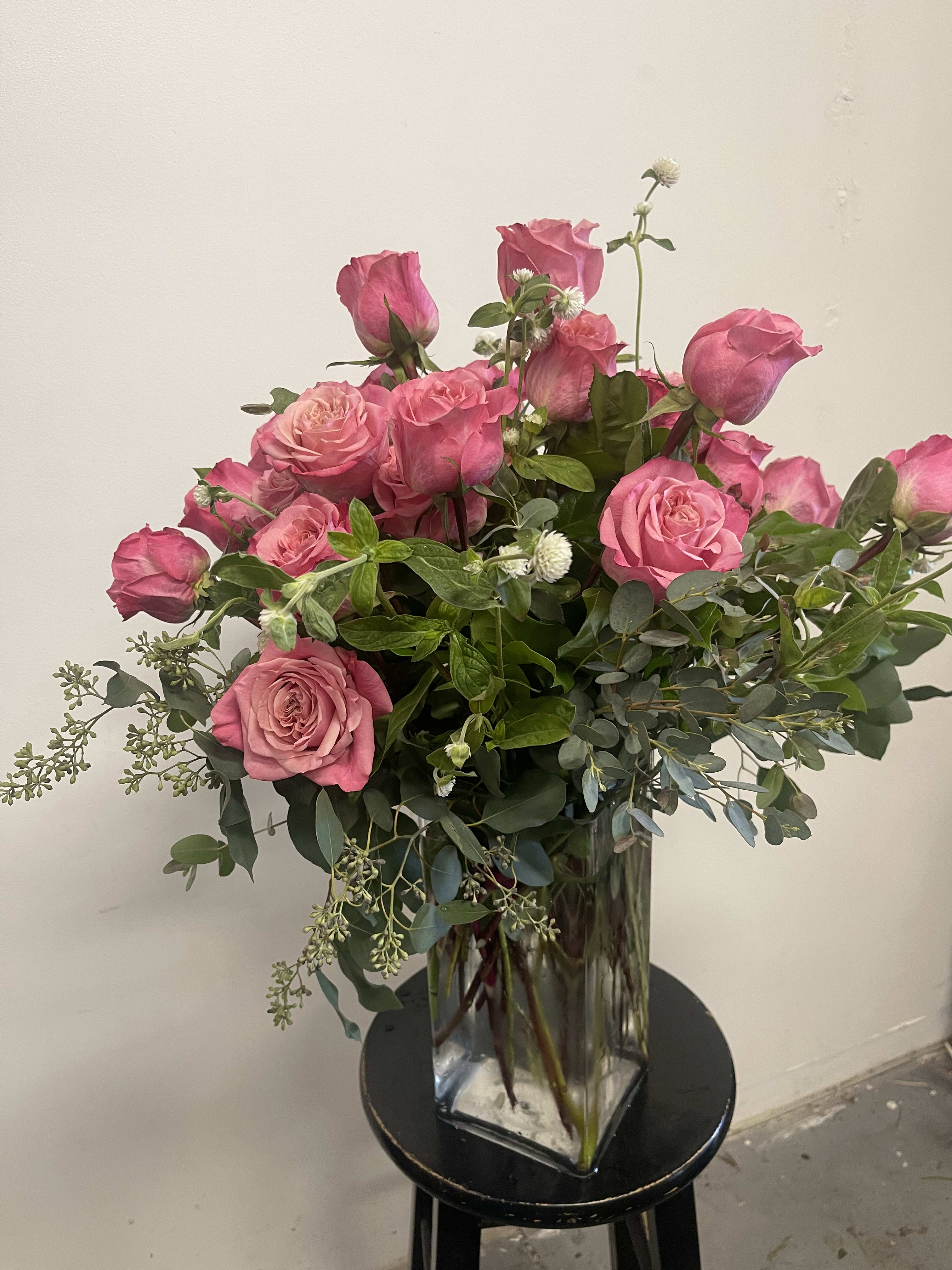 Pink roses arranged in a clear glass vase with greenery