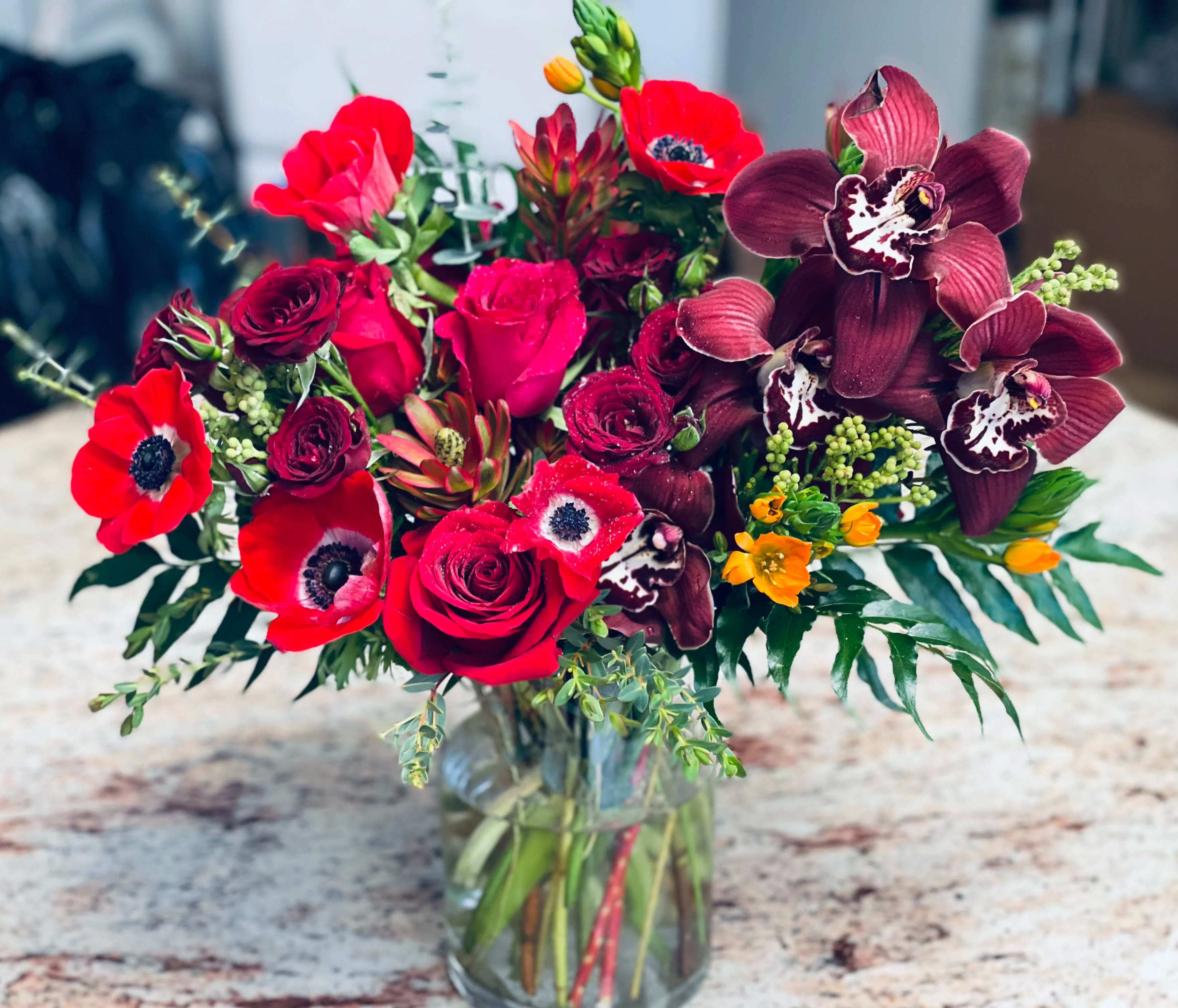 Bouquet of red roses and dark orchids in a glass vase