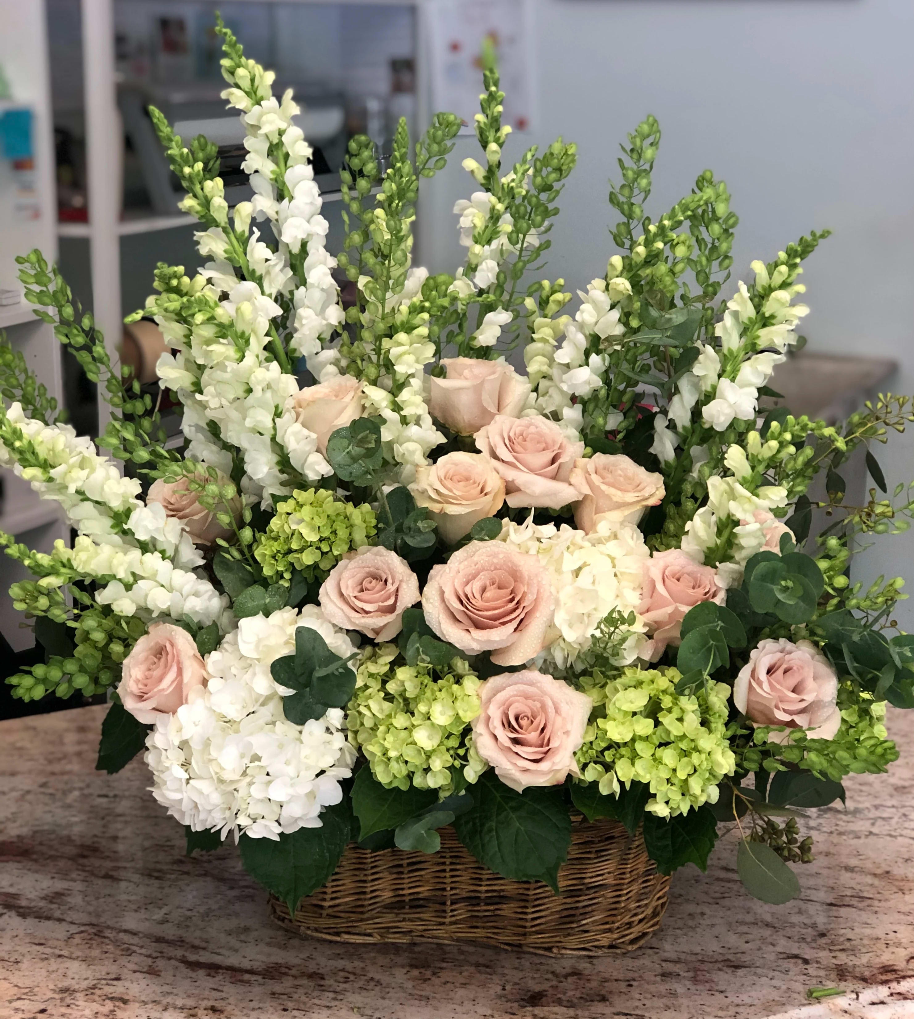 Basket arrangement of pale pink roses and white snapdragons with hydrangeas