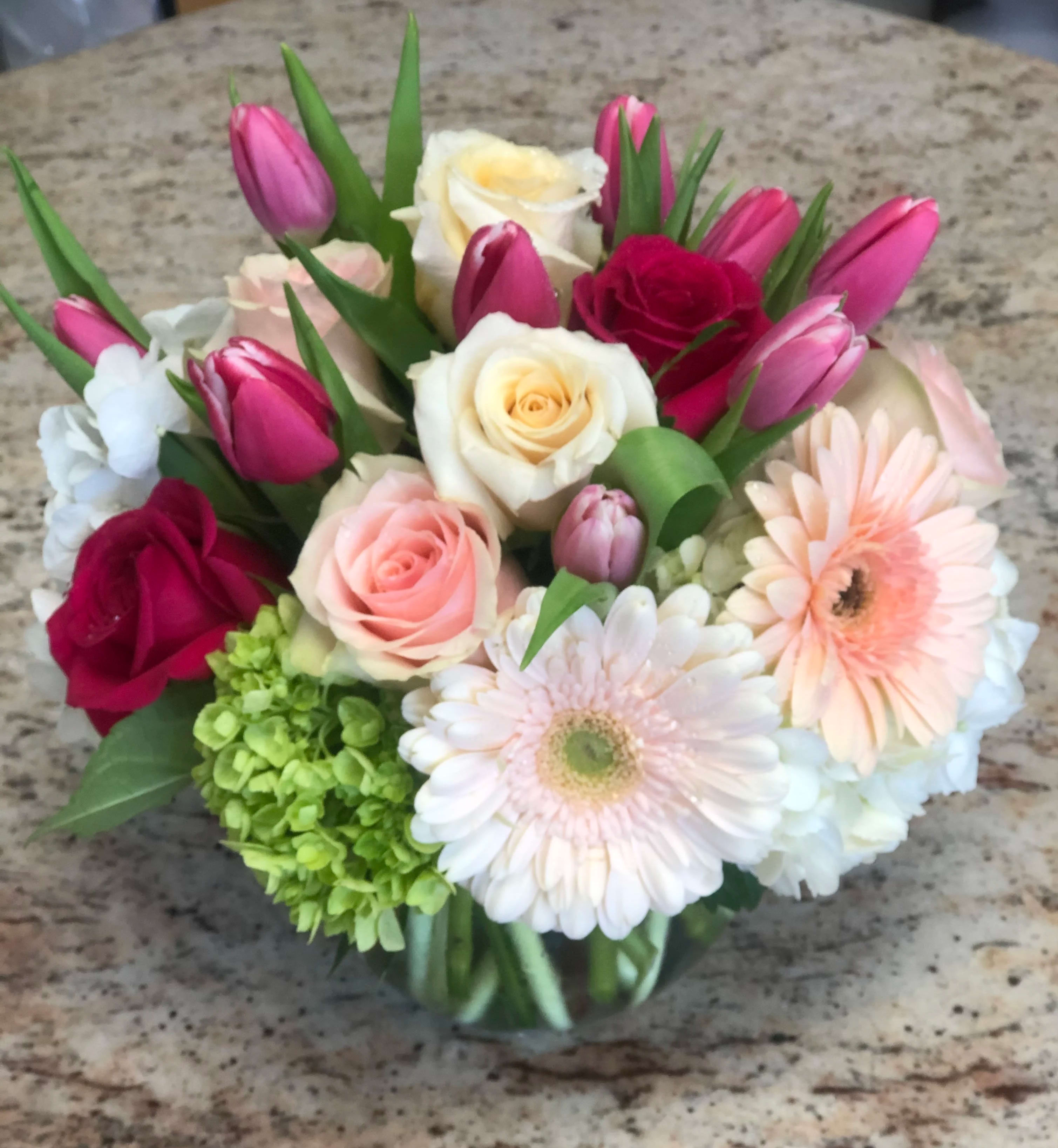Mixed bouquet of roses, tulips, hydrangea, and gerbera daisies in a glass vase