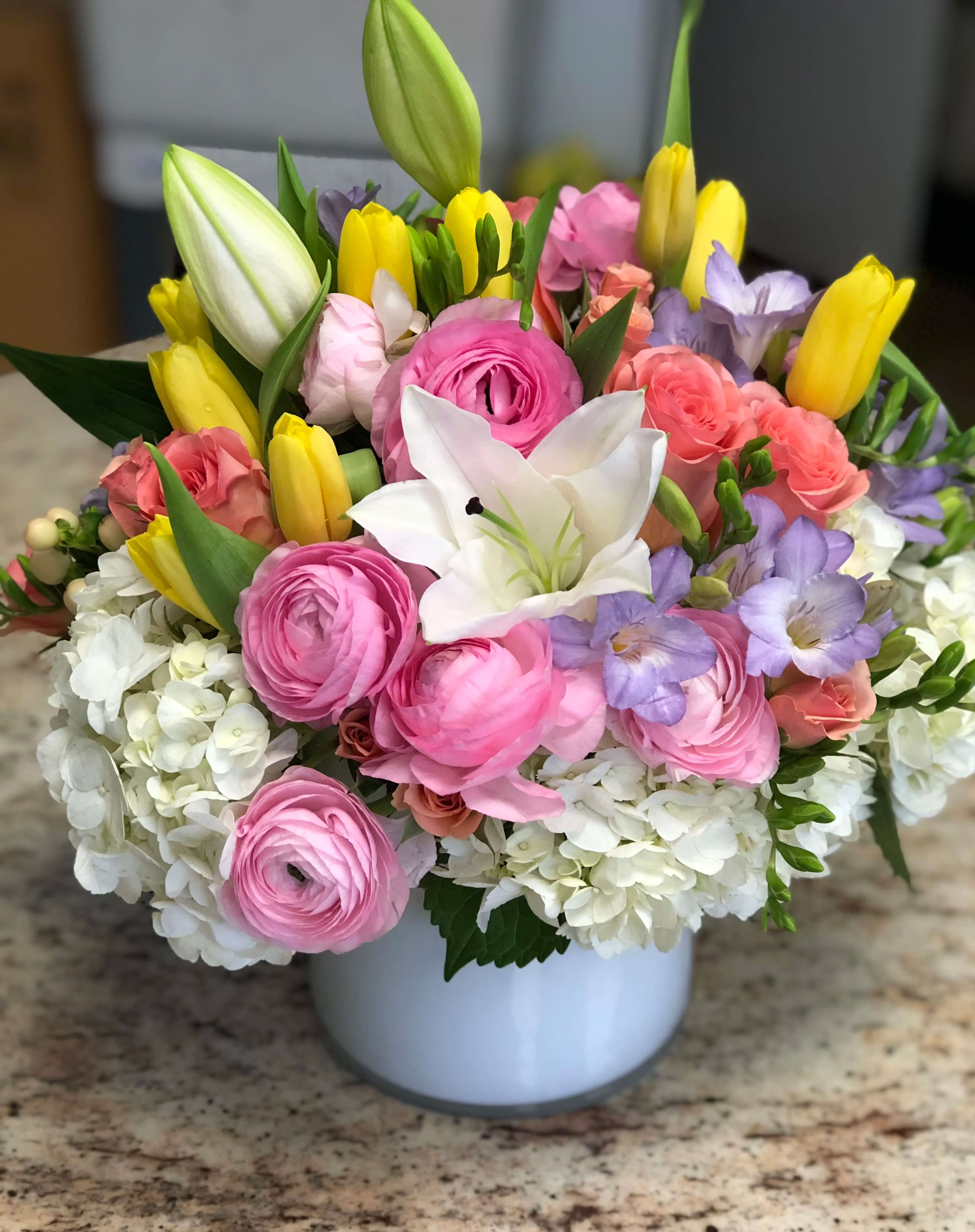 Mixed bouquet of pink, white, yellow, and lavender flowers in a white vase