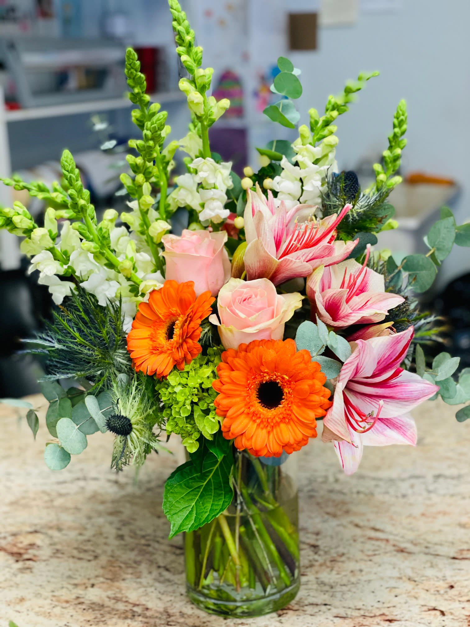 Mixed bouquet with orange gerbera daisies, pink roses, and striped lilies in a glass vase