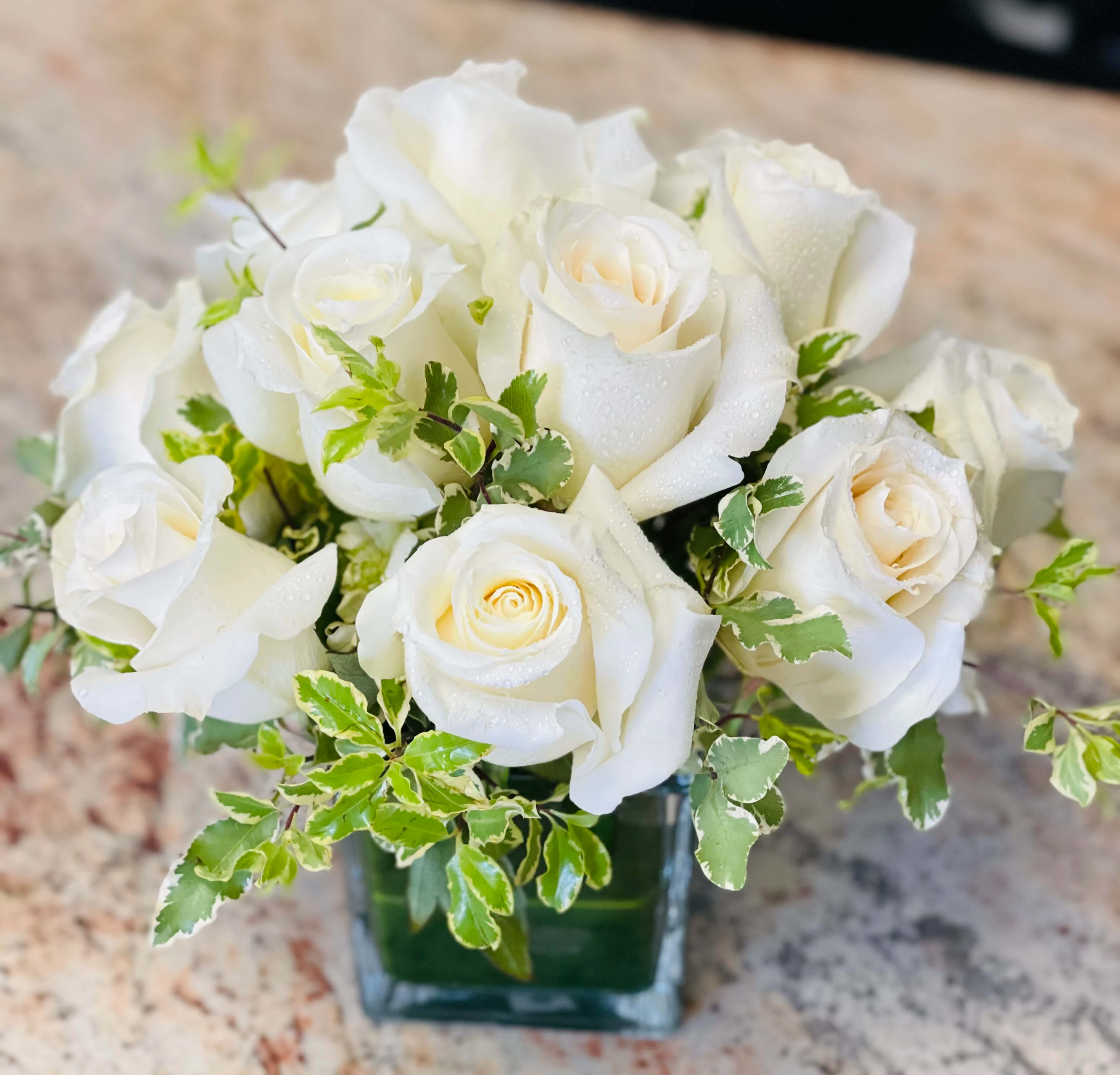 White rose bouquet in a square glass vase with variegated greenery