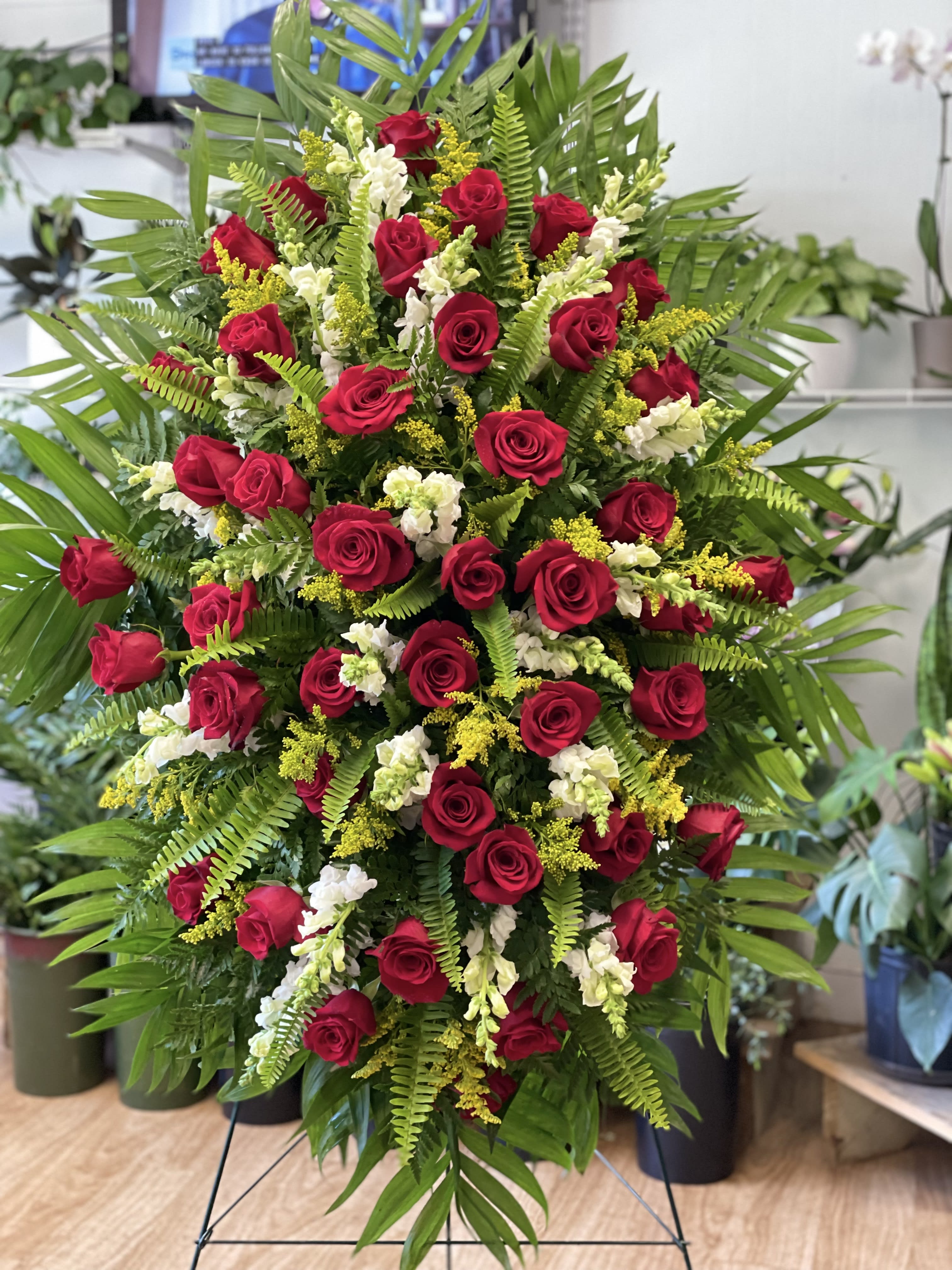 Tall standing spray of red roses with white flowers and yellow accents on lush greenery.