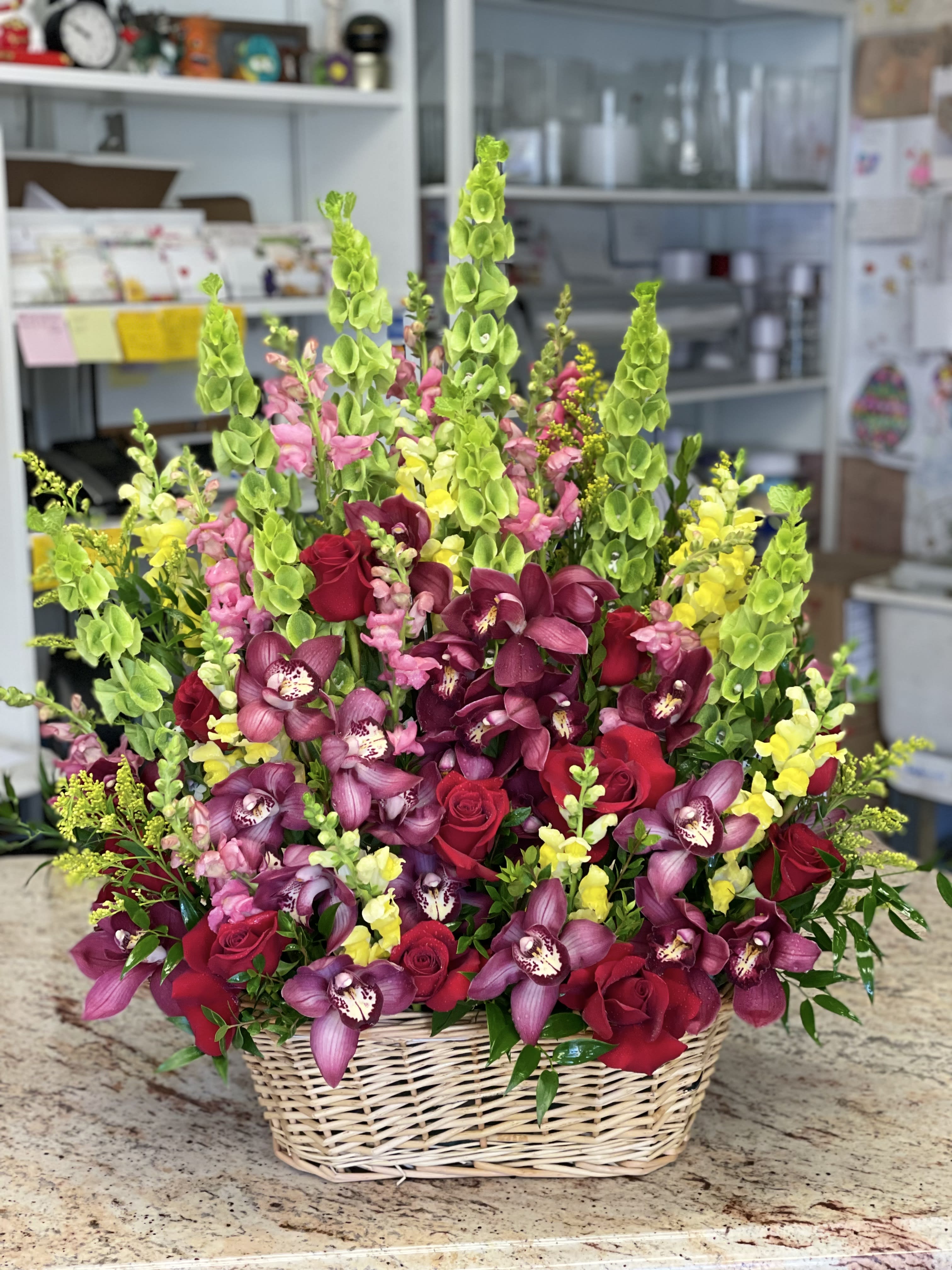 Basket arrangement of red roses, purple orchids, and green snapdragons