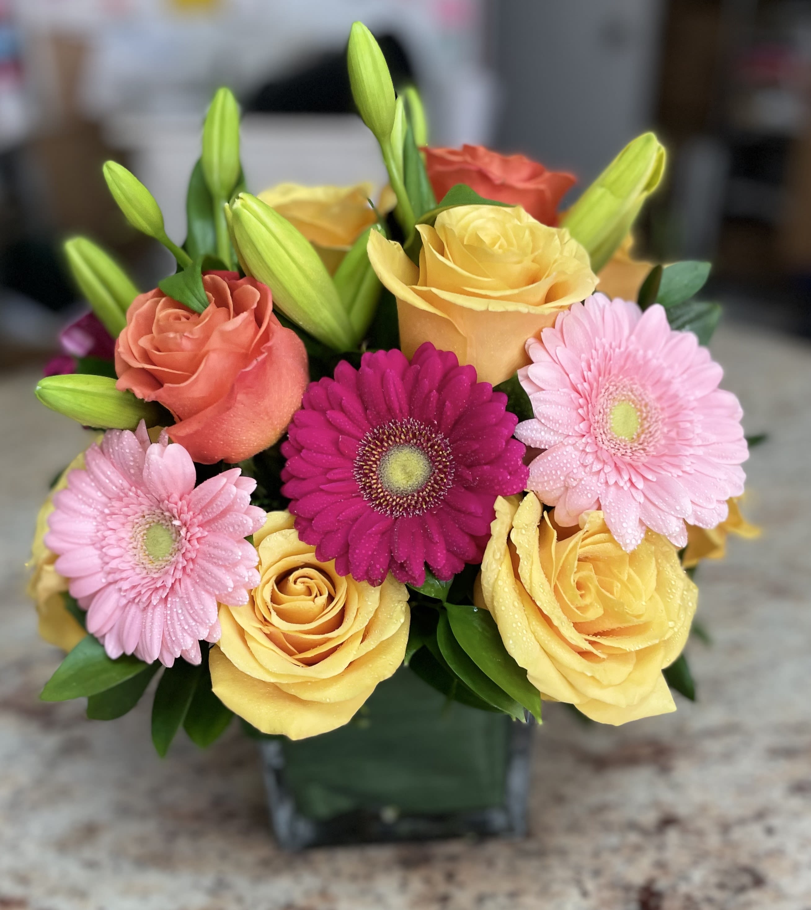 Mixed bouquet of roses, gerbera daisies, and lilies in a glass vase