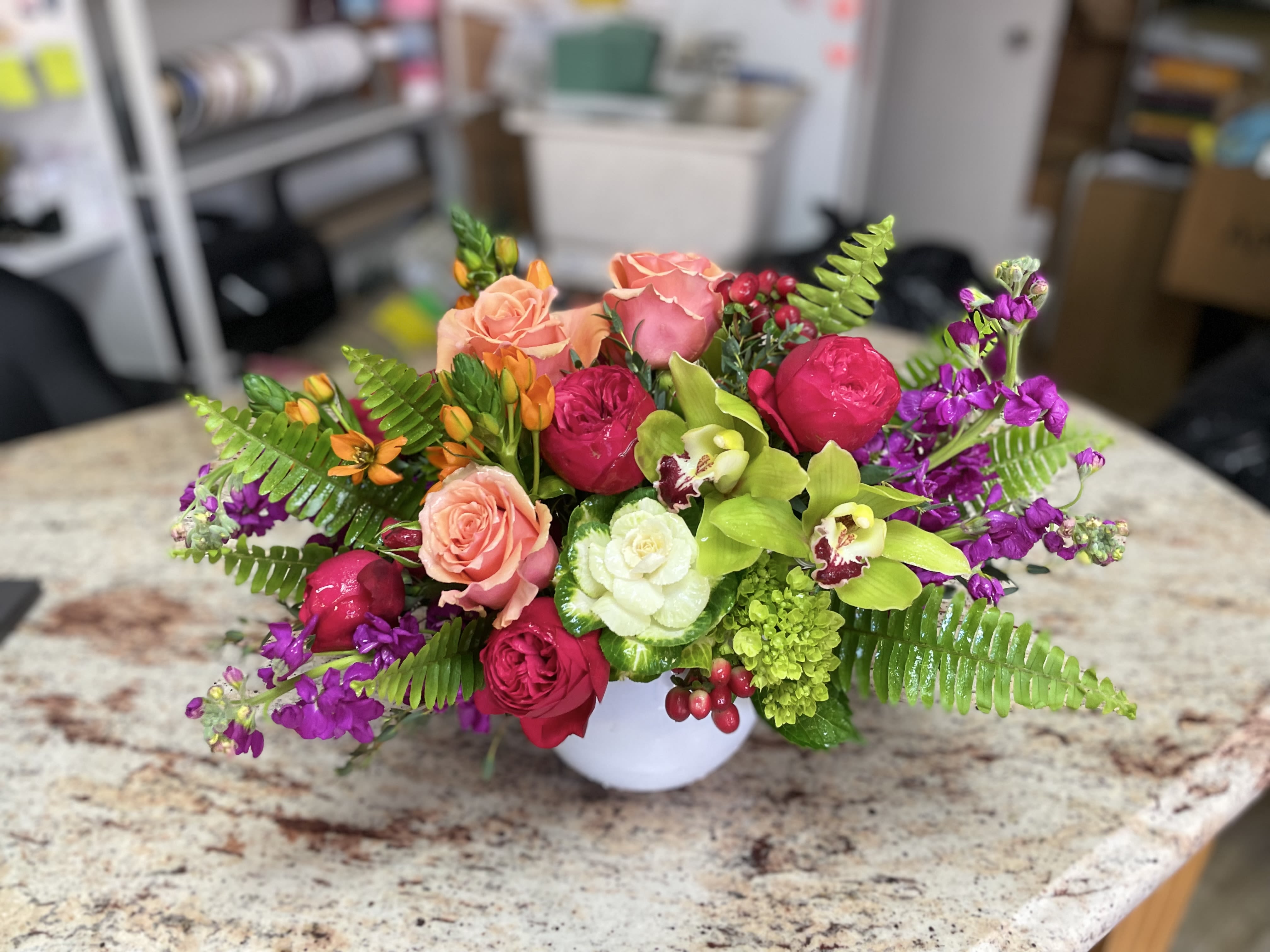 Mixed bouquet of roses, orchids, and purple flowers in a white vase