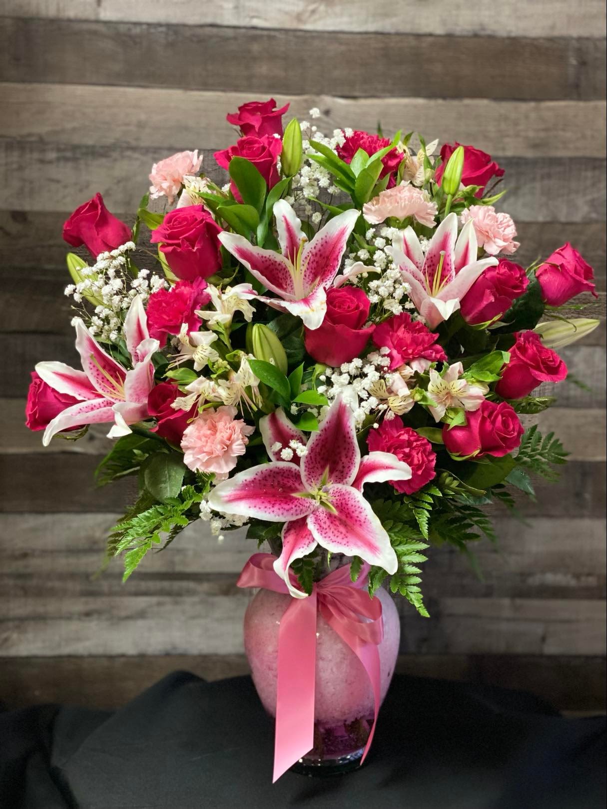 Pink roses and lilies arranged in a glass vase with a ribbon.