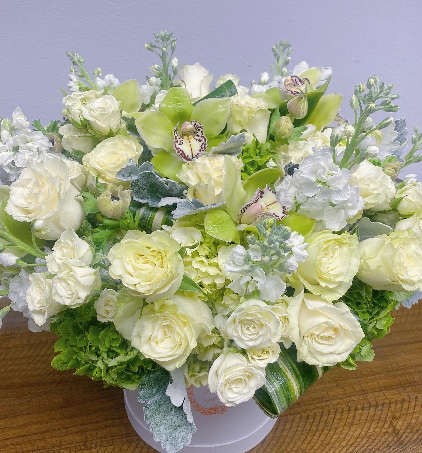 White and pale green floral arrangement in a round box