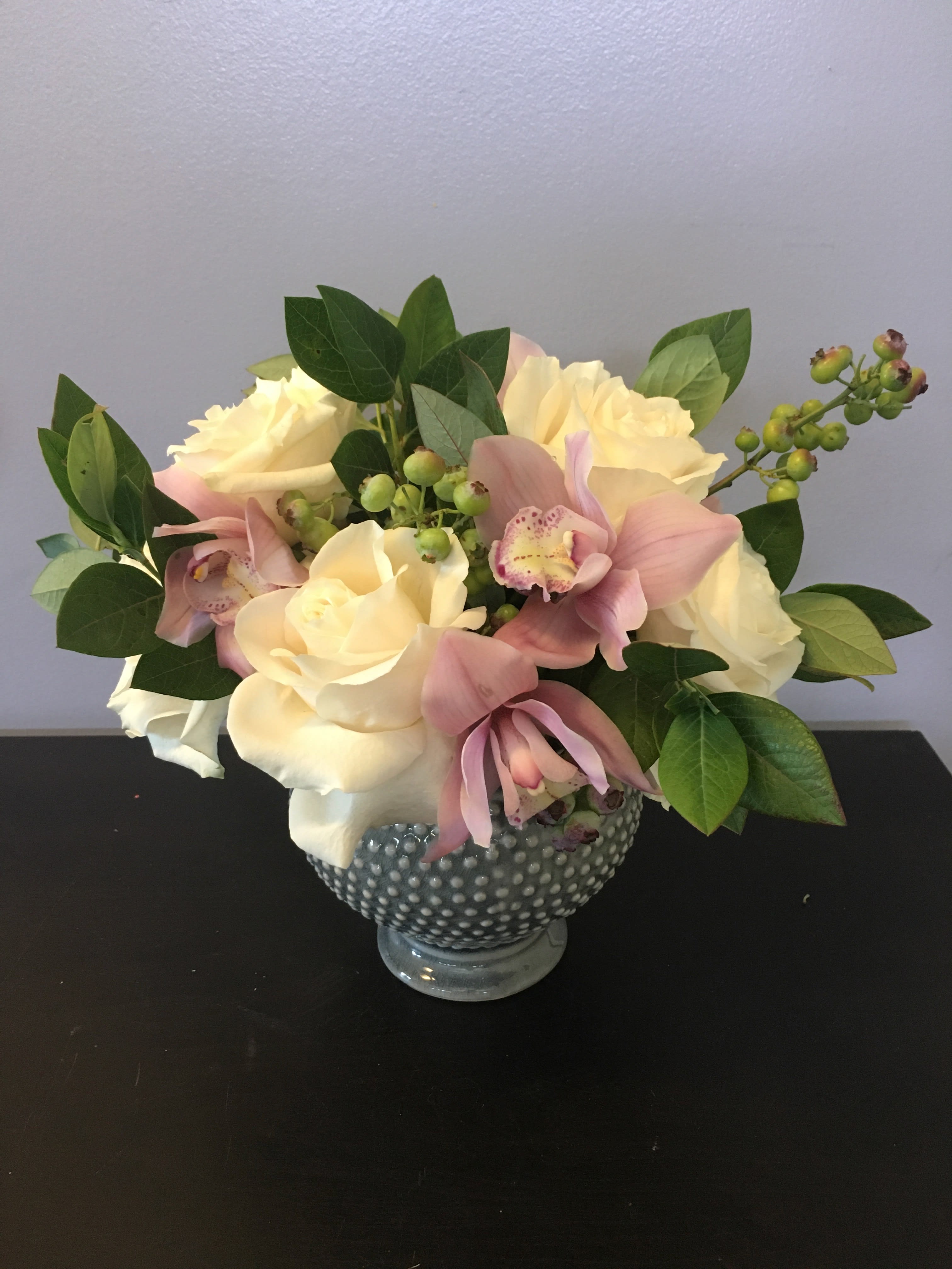 Cream roses and pink orchids arranged in a dotted glass vase