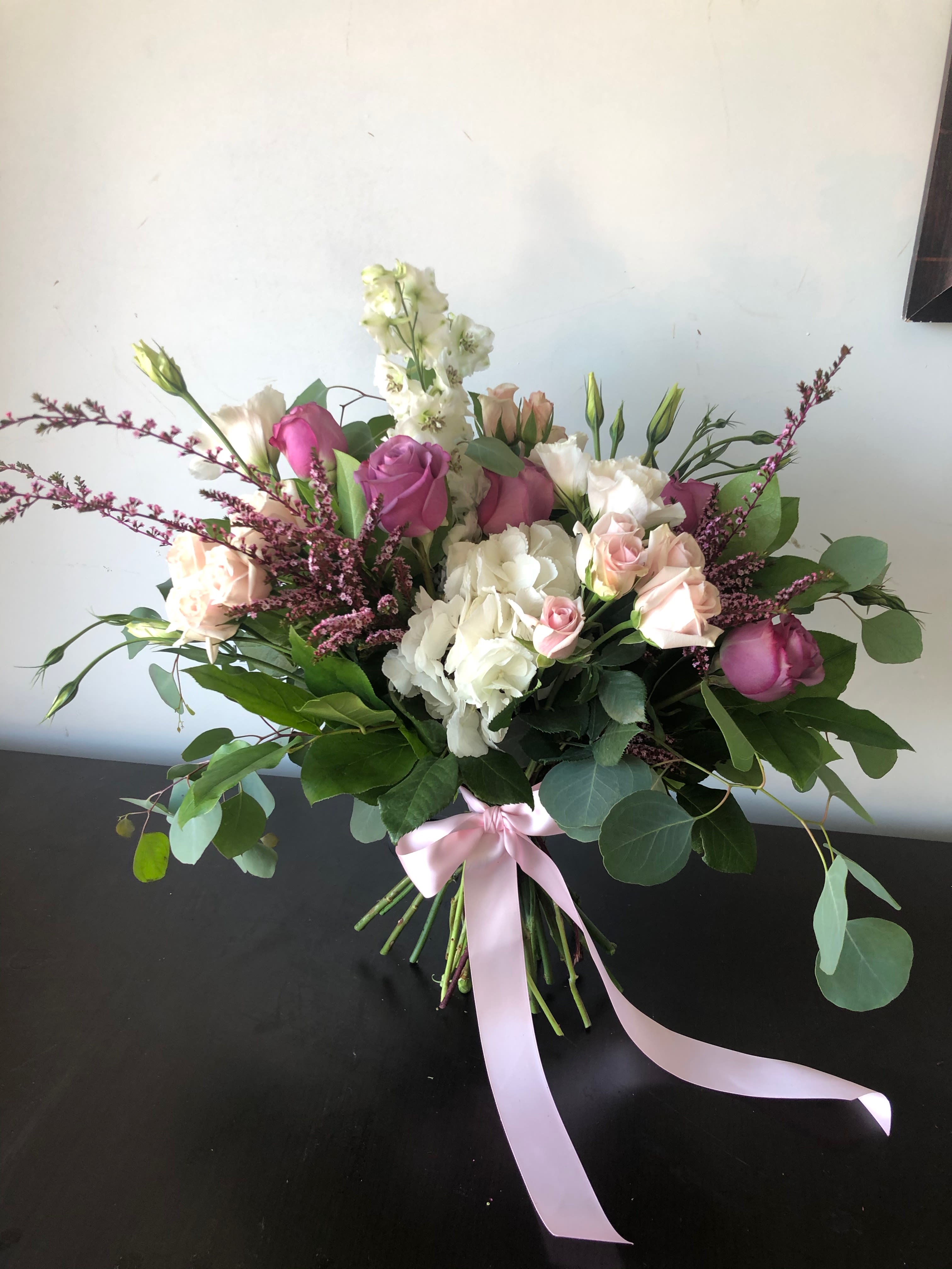 Bouquet of pink and white roses with greenery tied with a pink ribbon