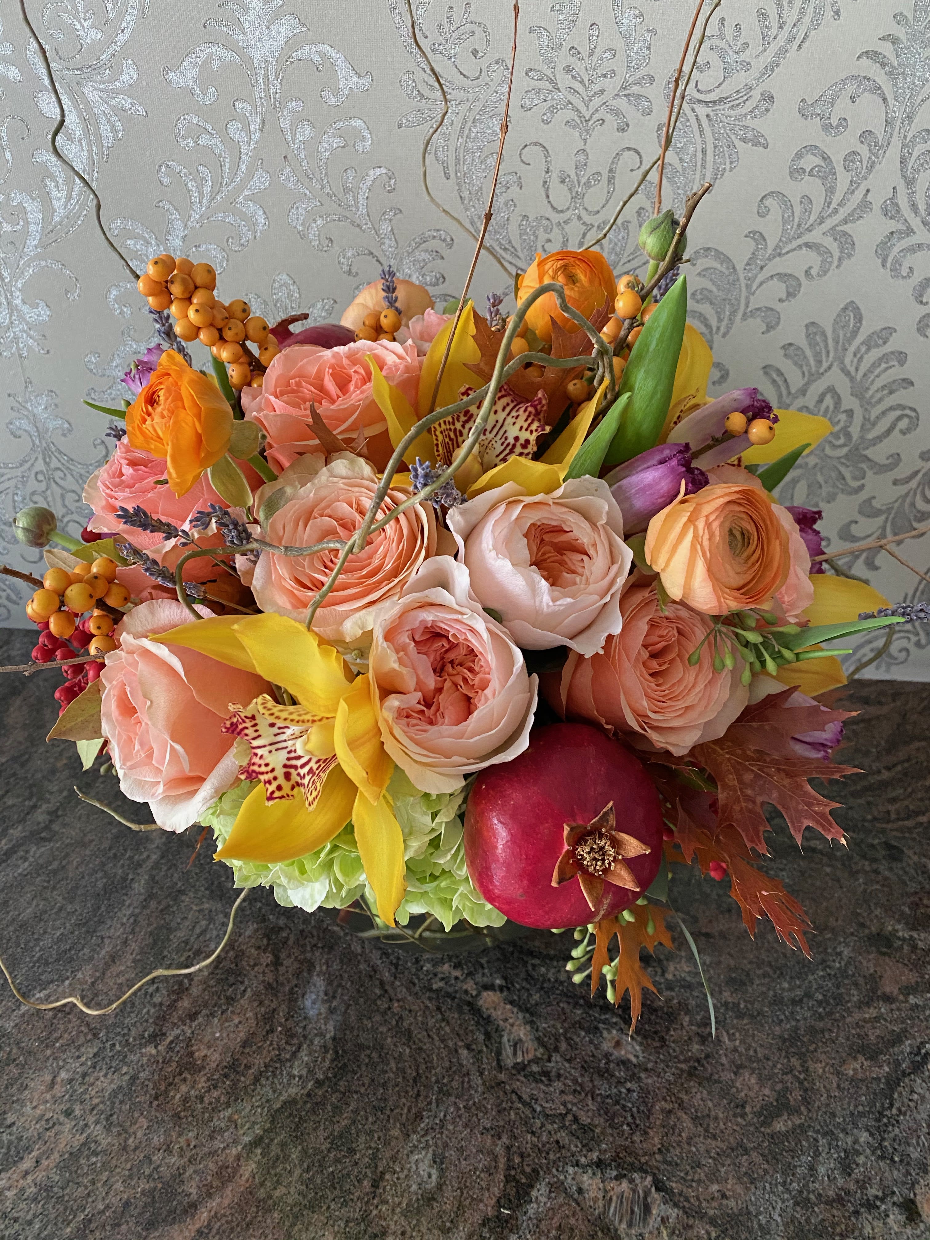 Mixed bouquet of peach roses, yellow orchids, and a pomegranate