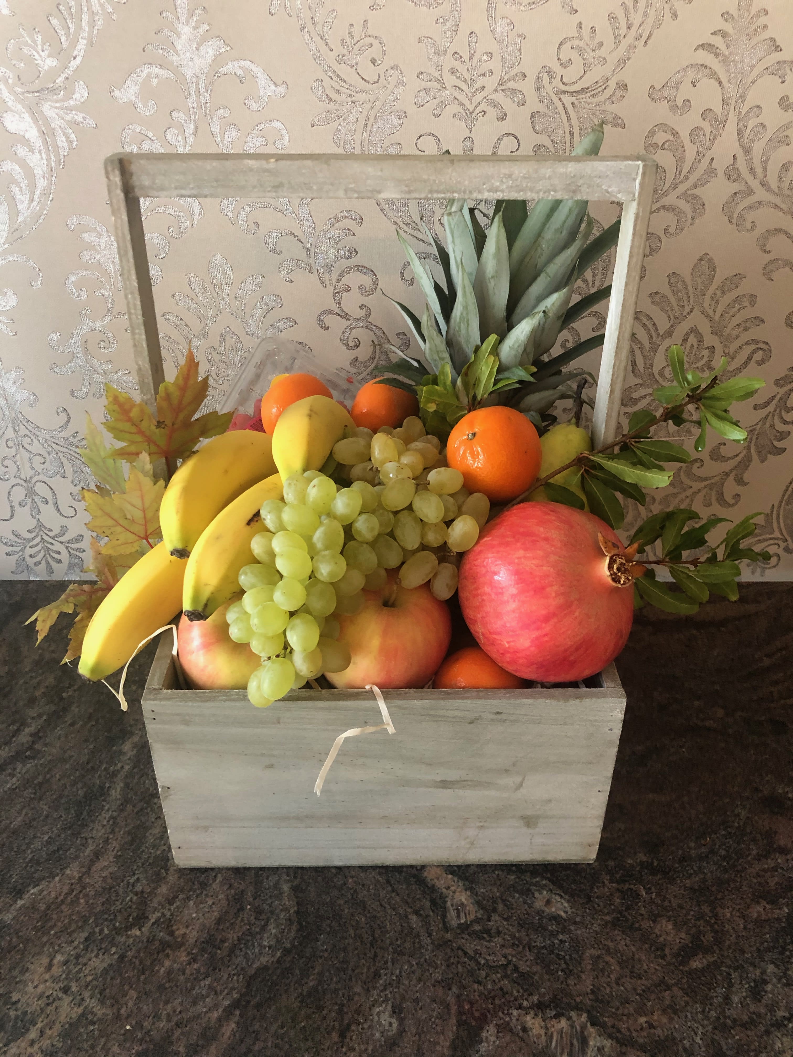 Wooden crate filled with assorted fruit including bananas, grapes, oranges, and pomegranates