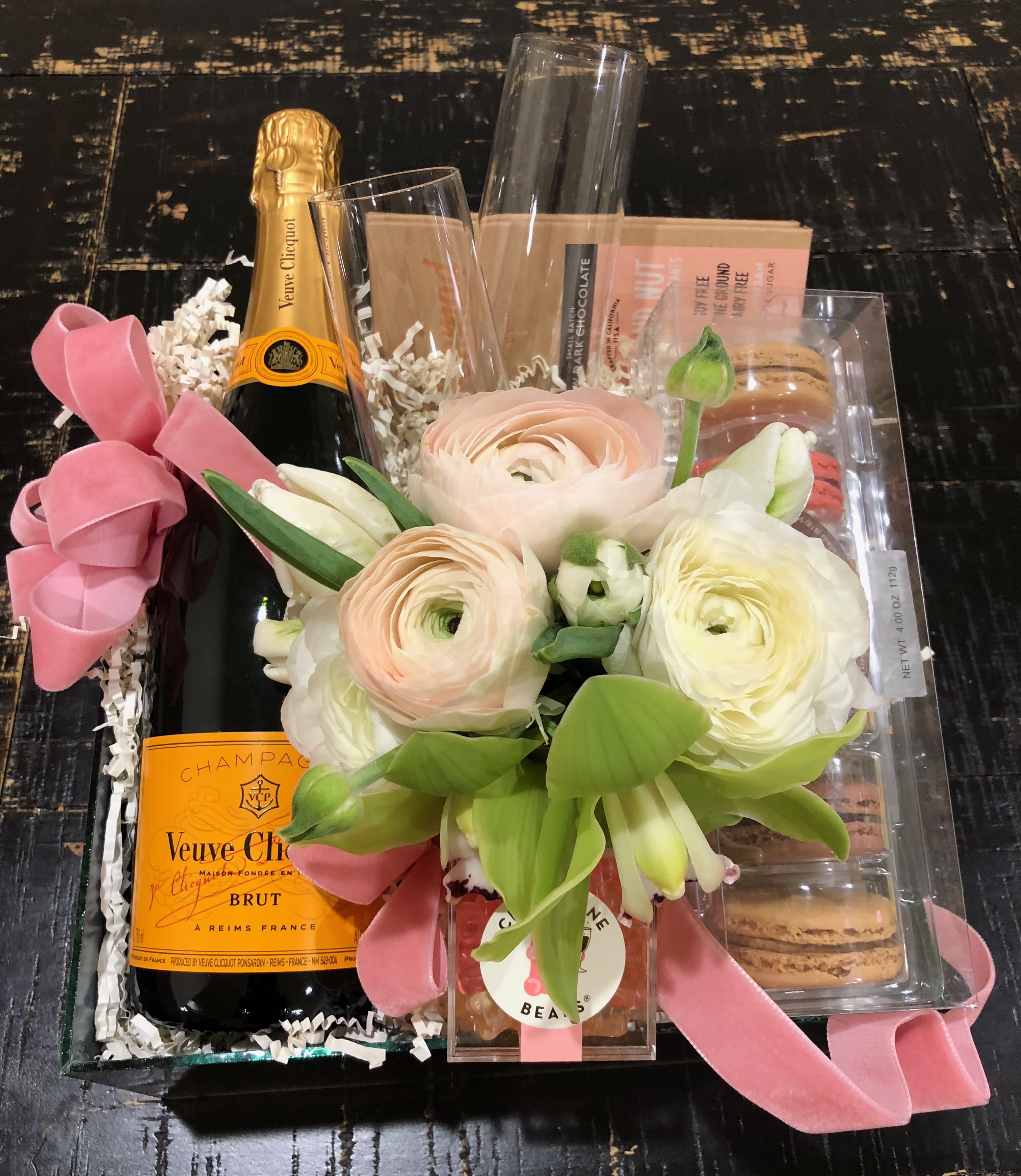 Gift basket with flowers, champagne, macarons, and candy in a clear tray