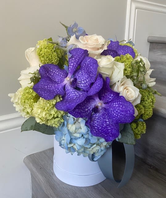 Bouquet of purple orchids, white roses, and blue hydrangeas in a white hat box