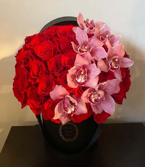Red roses and pink orchids arranged in a black hatbox