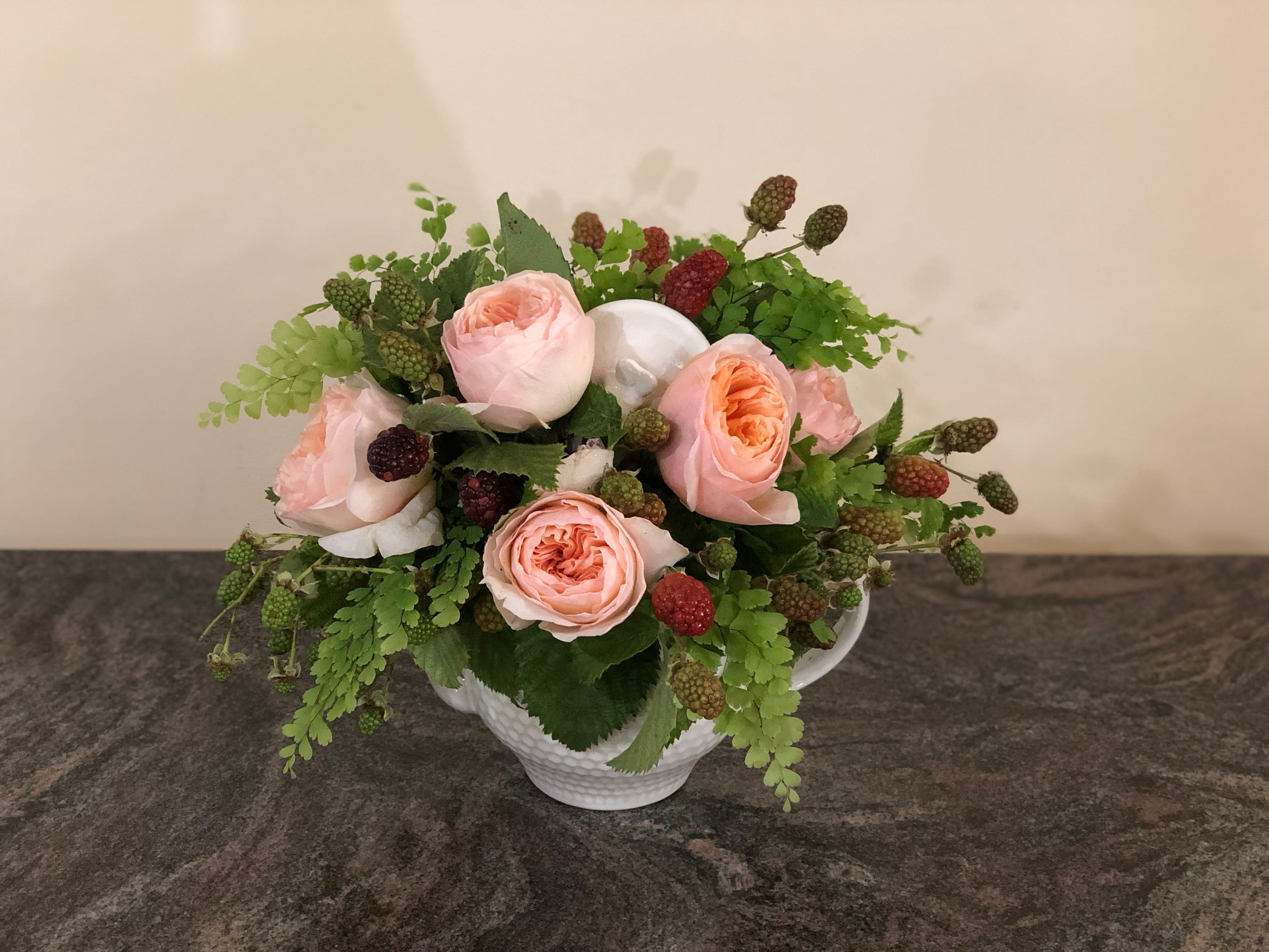 Pink roses arranged in a white teacup vase with green berries and foliage