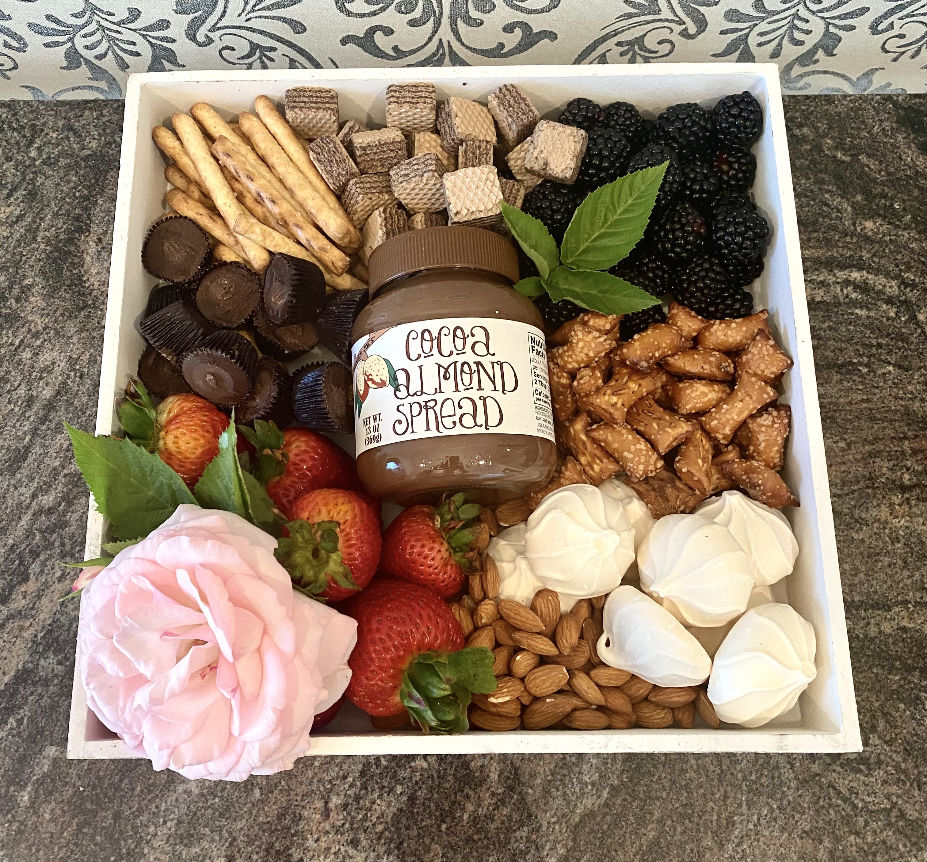 Gift tray with fruit, chocolates, crackers, nuts, and a pink rose