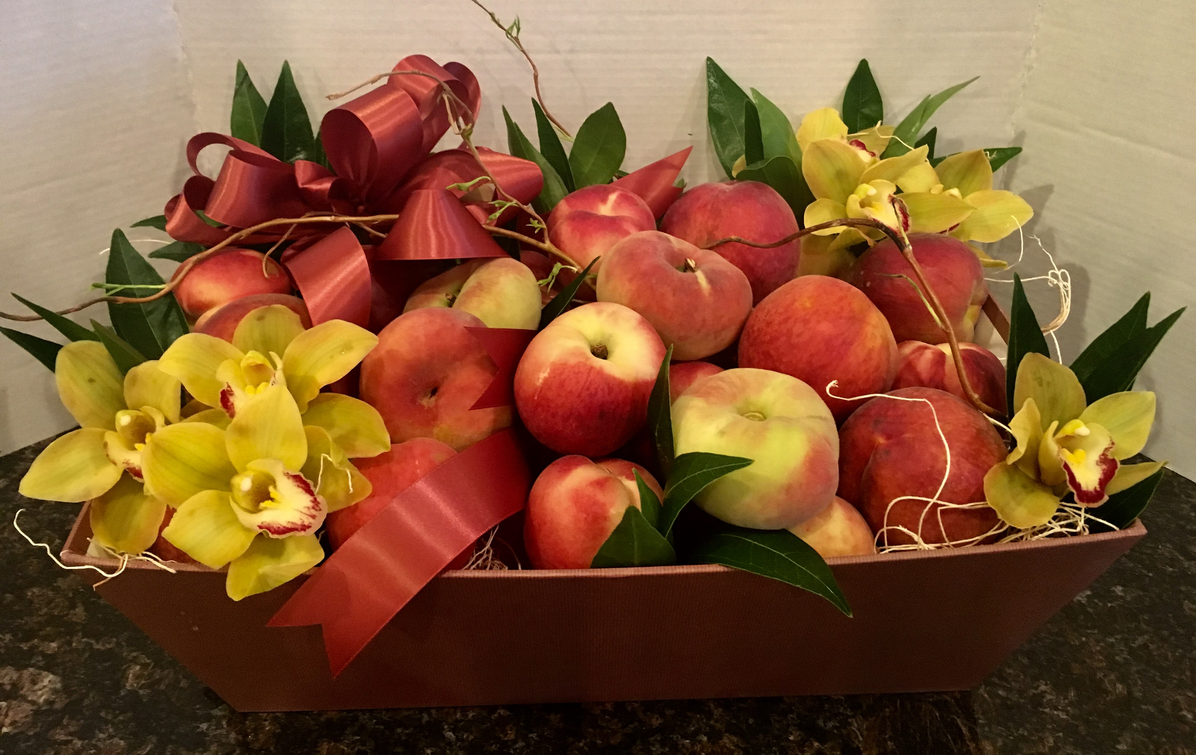 Fruit gift basket with peaches and yellow orchids in a brown tray