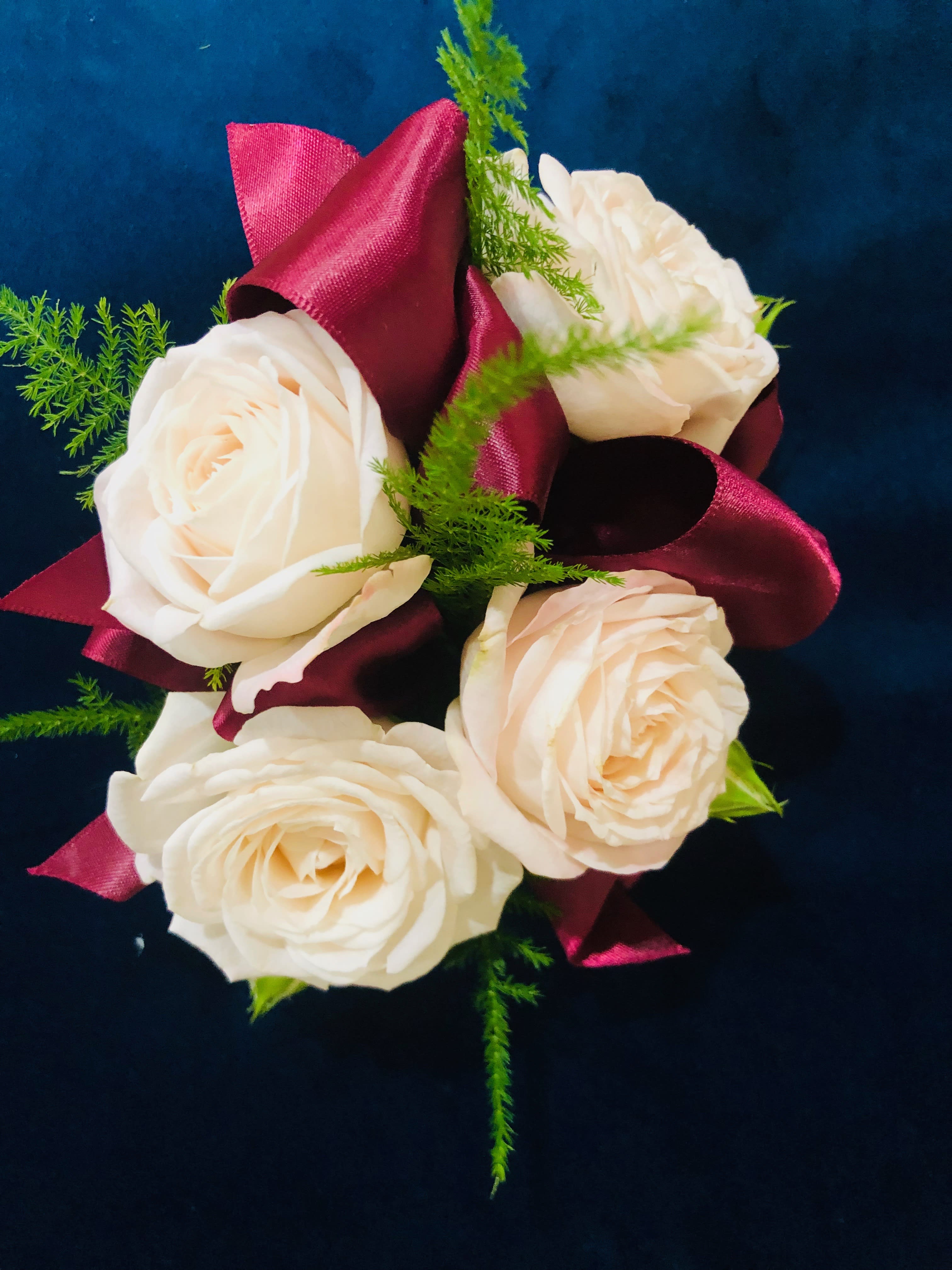 Cream roses with burgundy ribbon and green filler on a dark background