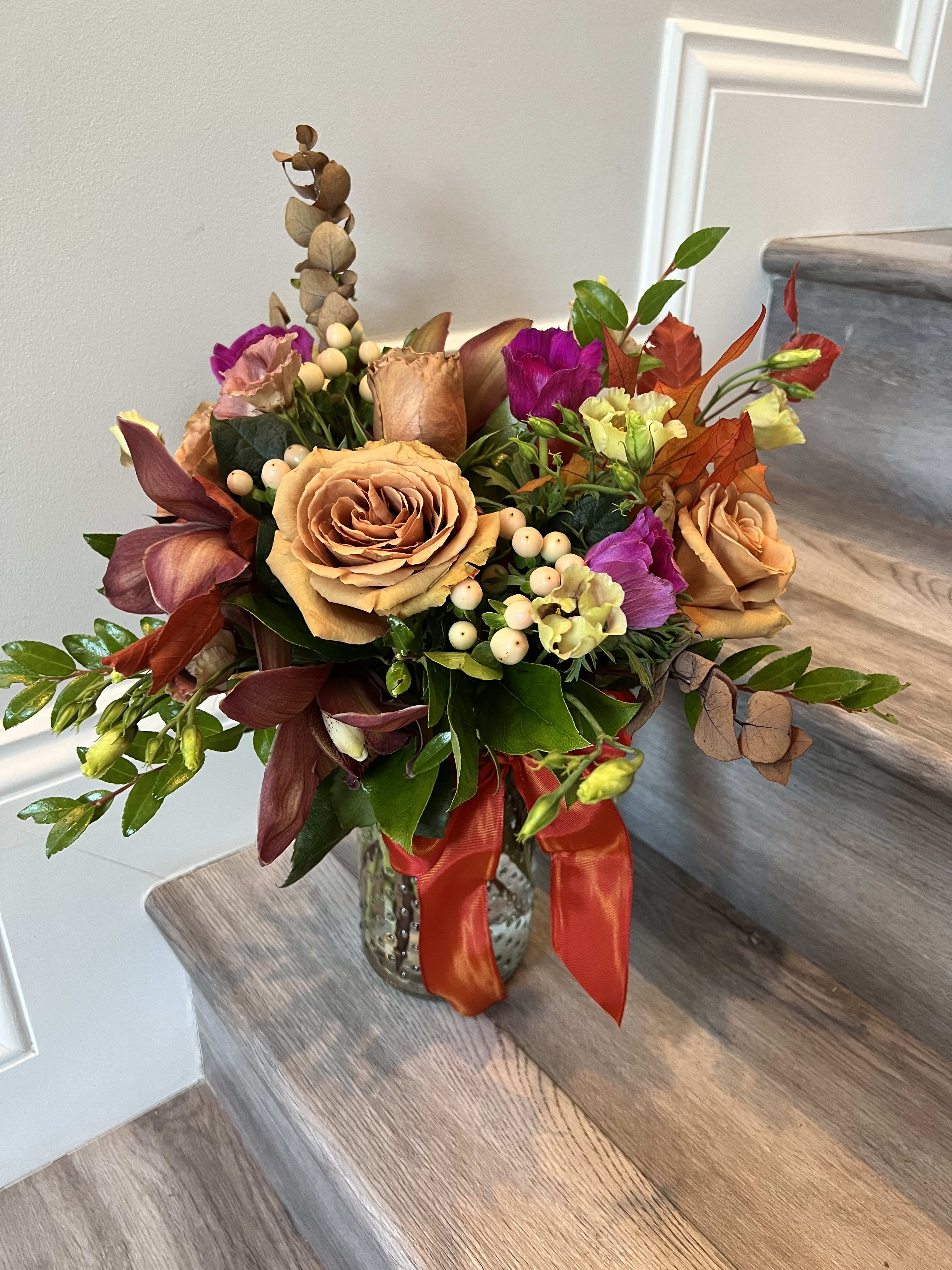 Mixed bouquet of peach roses and purple flowers in a glass vase with a red ribbon.