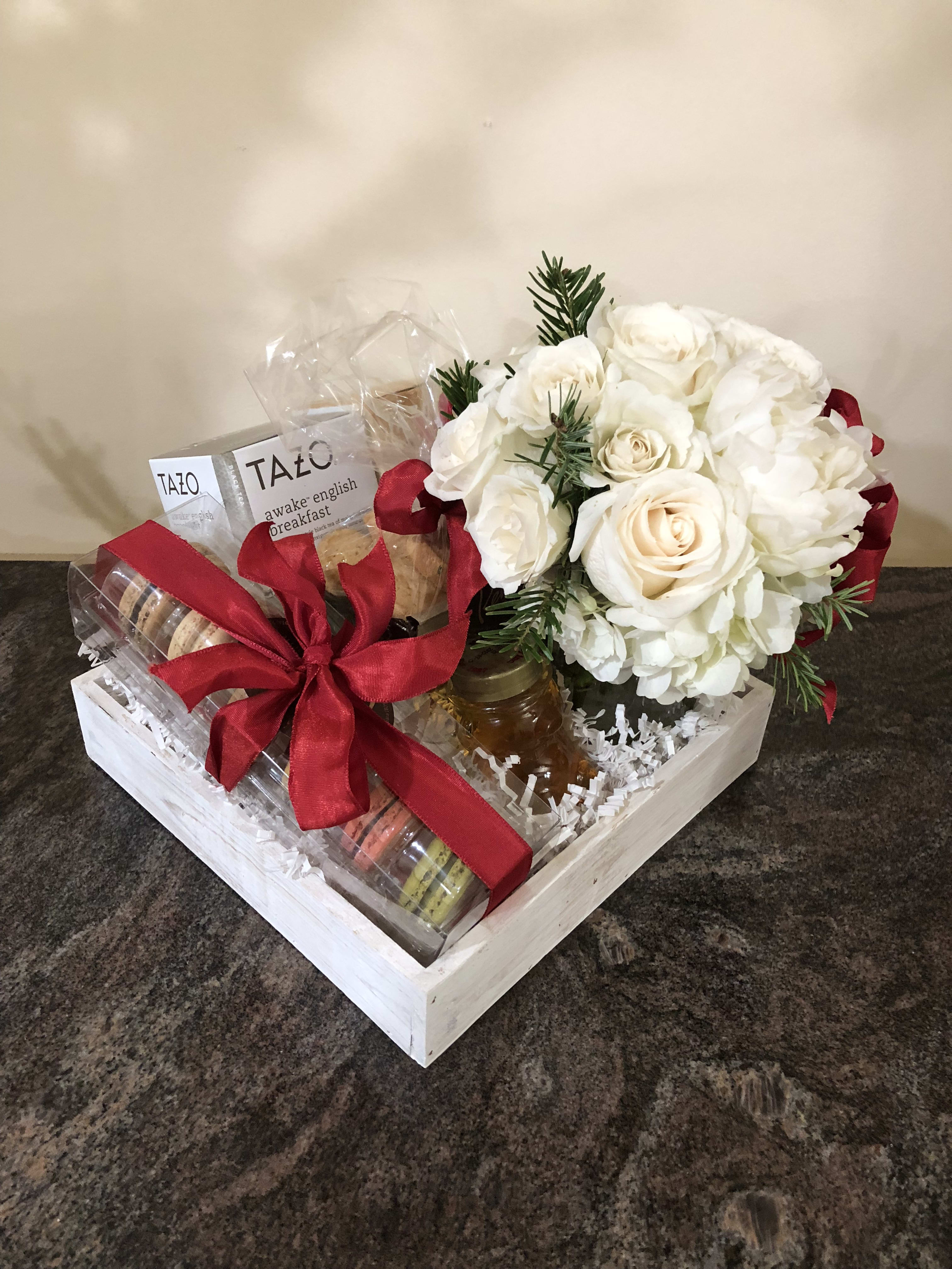 Gift basket with white roses, tea, cookies, and a red ribbon