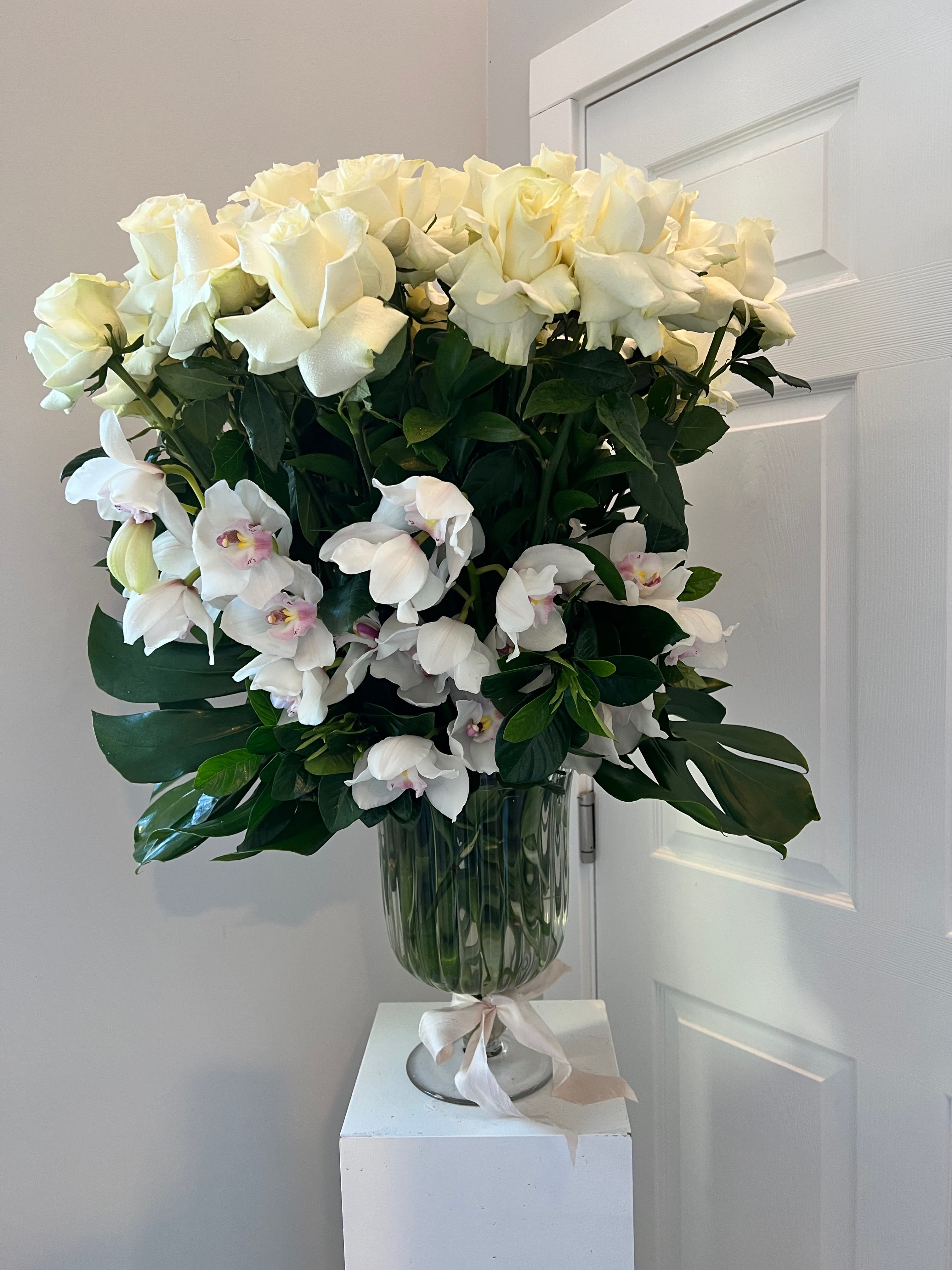 White roses and orchids arranged in a glass vase with a ribbon.