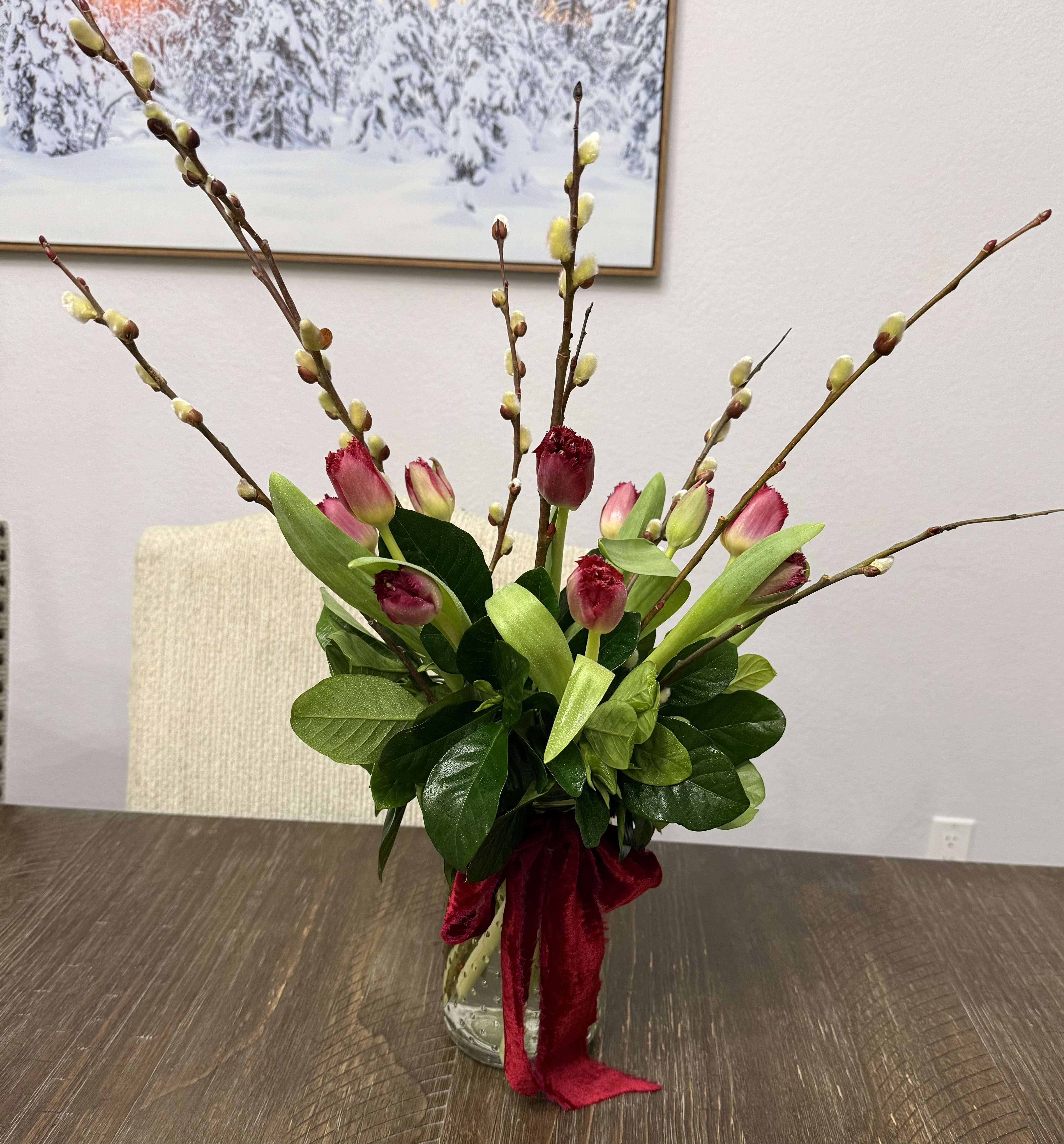 Pink tulips and pussy willow branches in a glass vase with a red ribbon